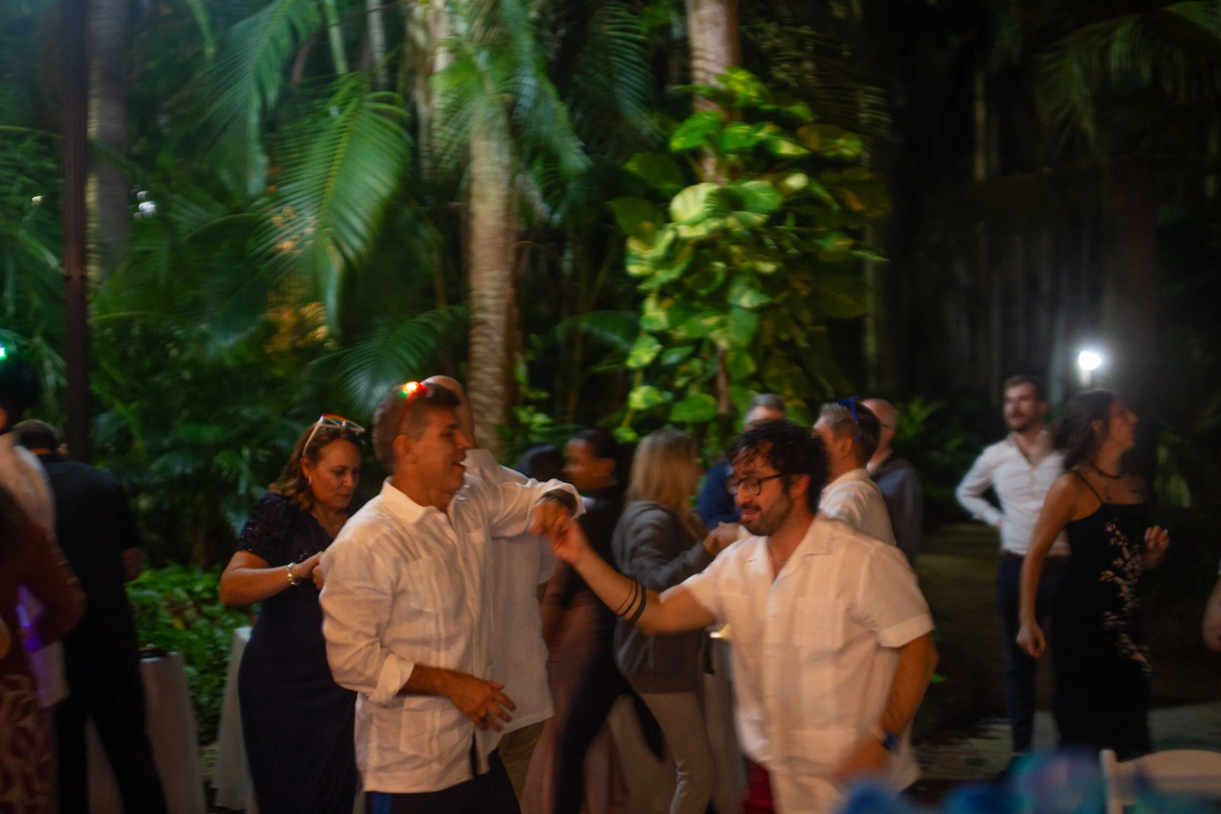 People dancing and socializing in a lush, tropical outdoor setting during the evening.