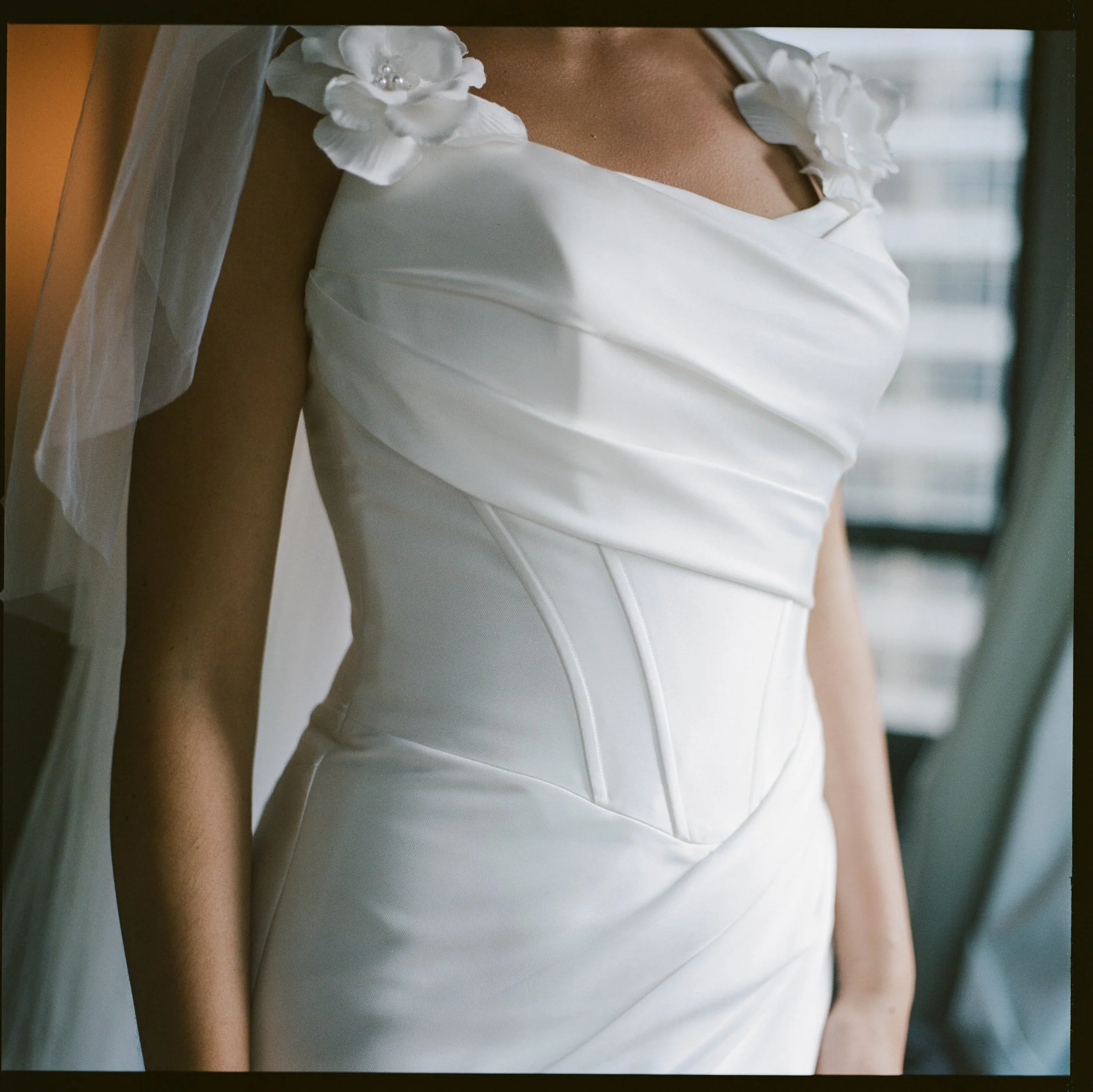 Close-up of a woman in a white wedding dress with floral details on the shoulder.