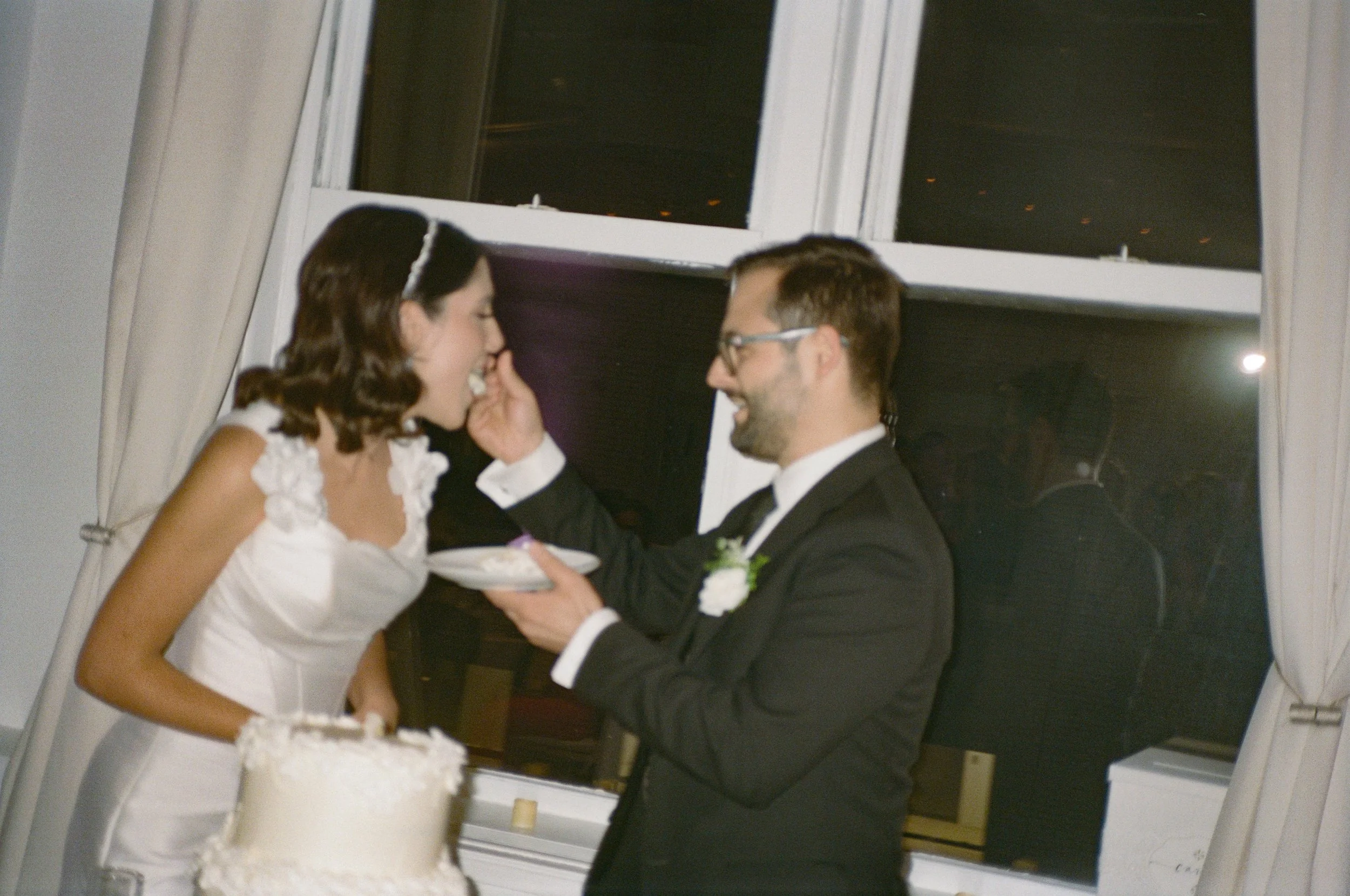 A bride and groom sharing a moment at their wedding reception, with the groom feeding the bride cake.