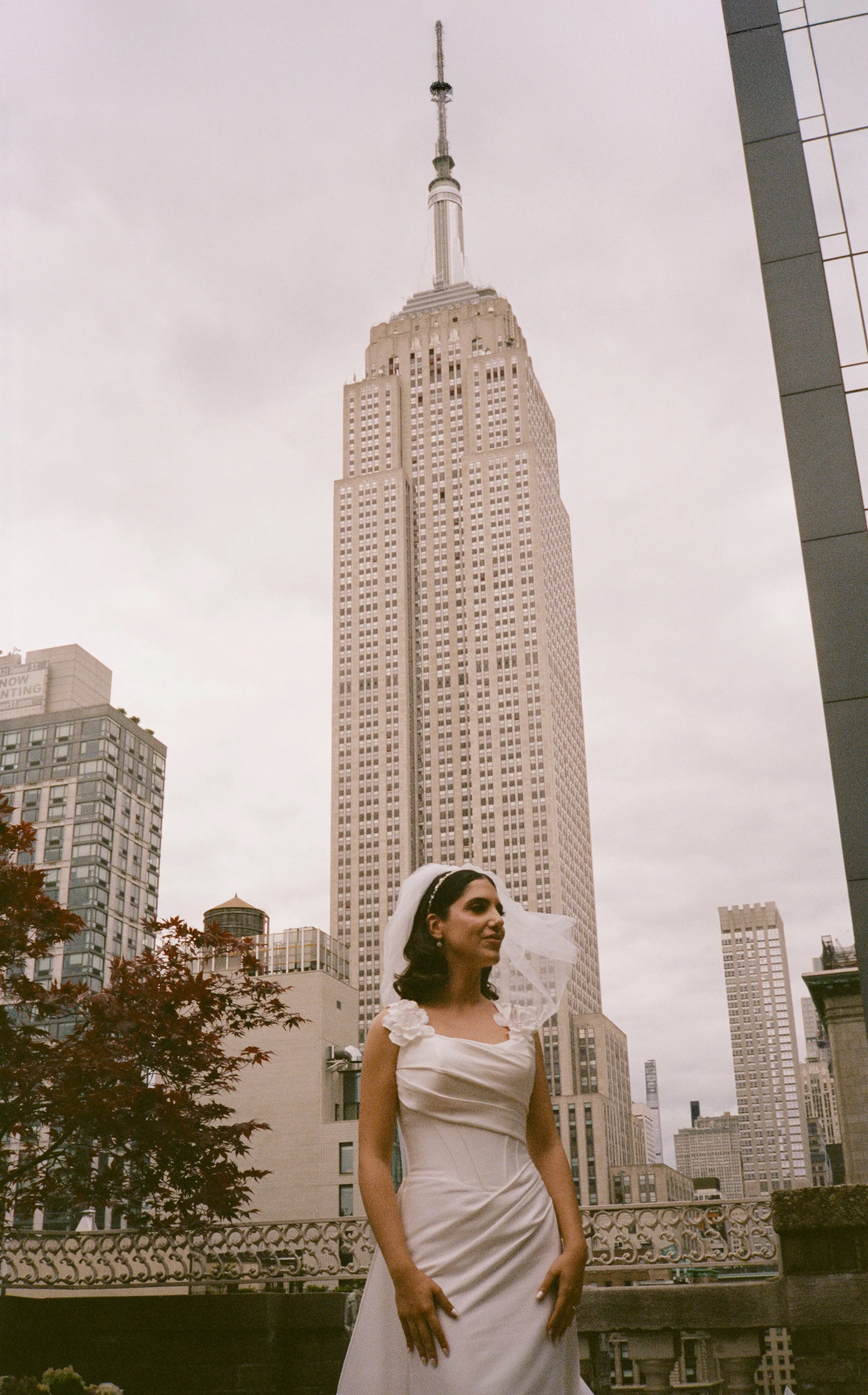 A woman in a wedding dress standing outdoors in front of the Empire State Building in New York City.