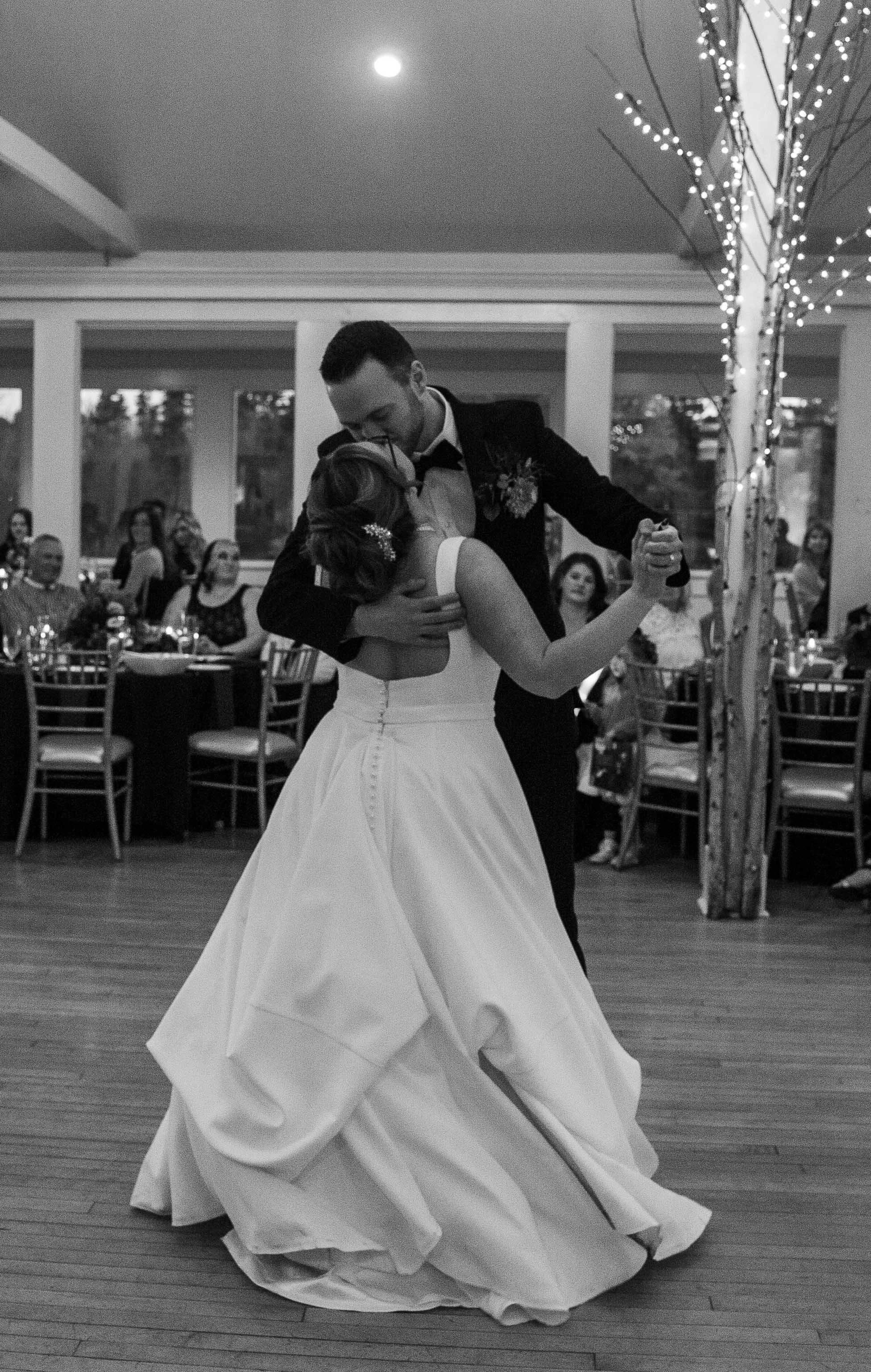 A bride and groom sharing a dance at their wedding reception, with guests seated at tables watching in the background.