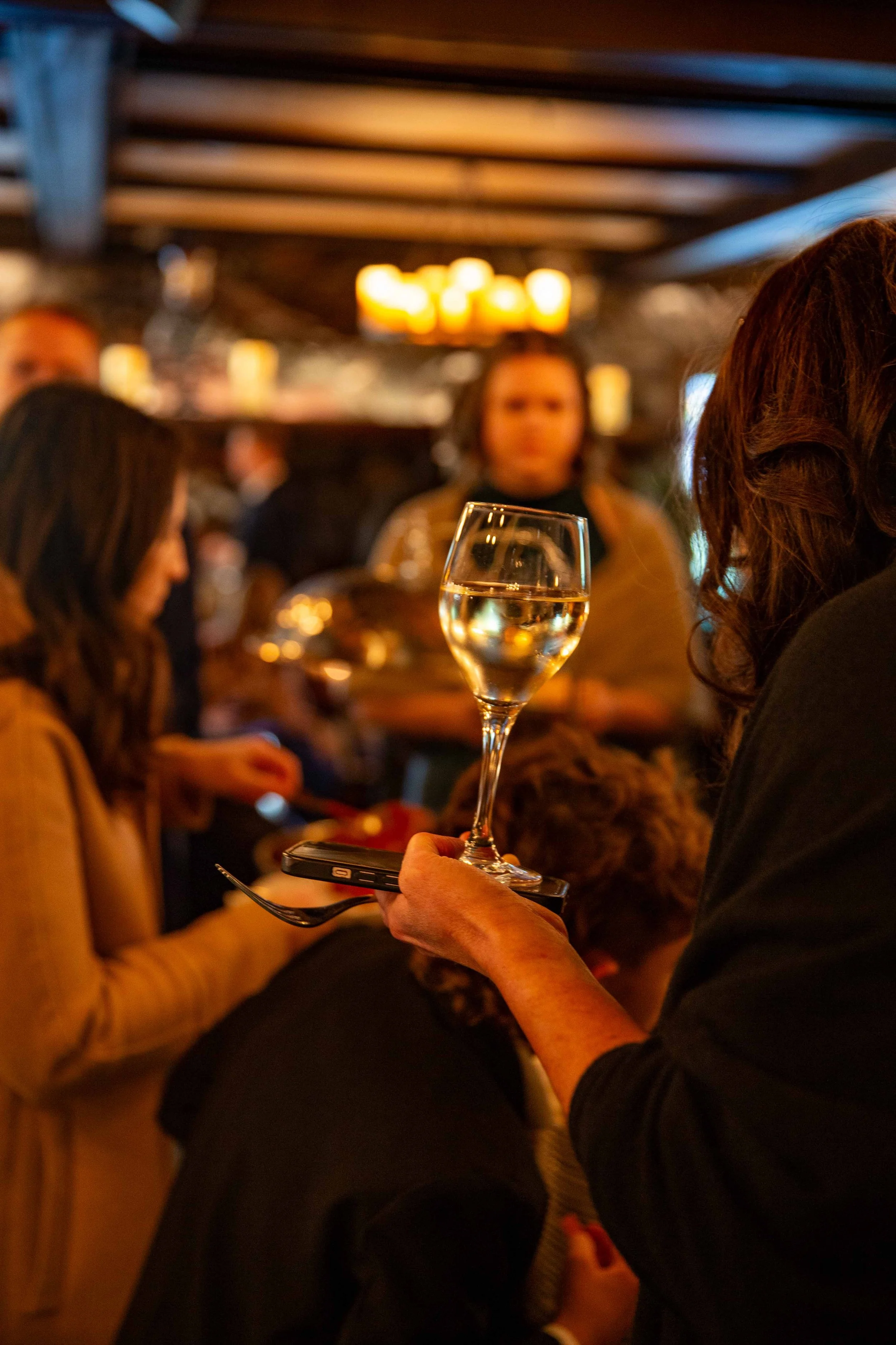 A woman holding a glass of white wine in a packed, dimly lit bar or restaurant.
