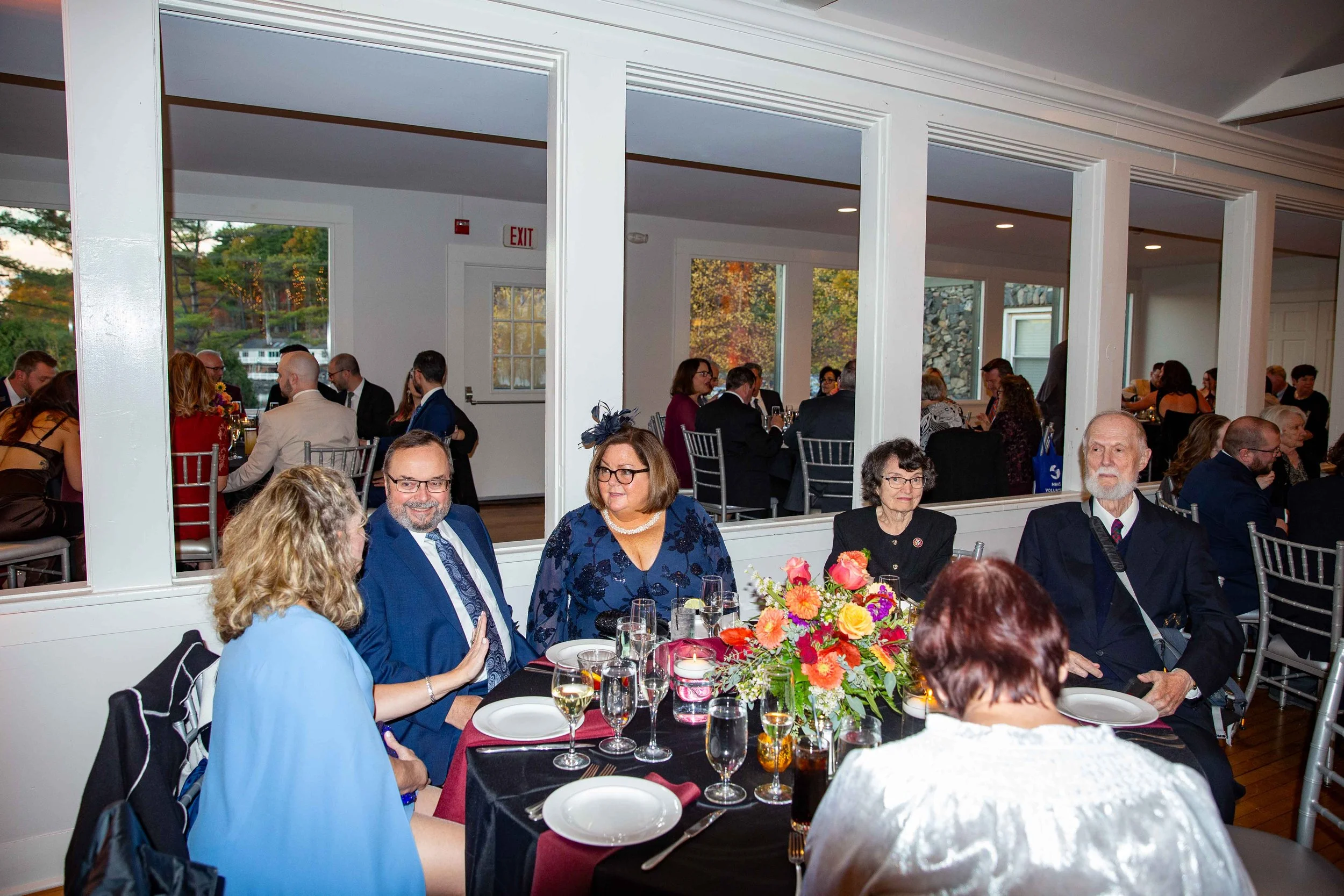 Guests seated at a formal dinner table with floral centerpiece, glasses, and plates during a celebration event