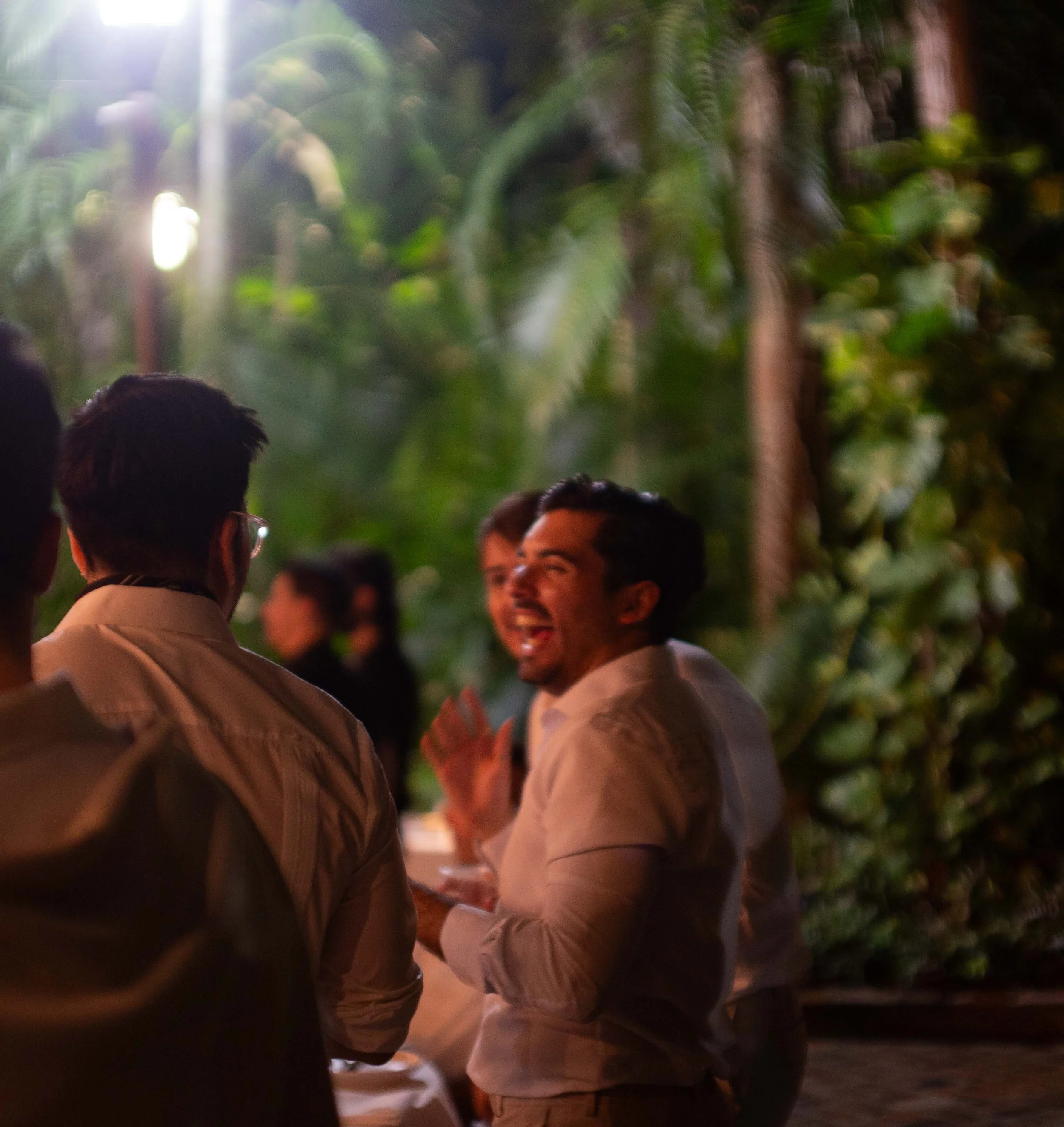 Group of people having a conversation outdoors at night, surrounded by lush greenery.