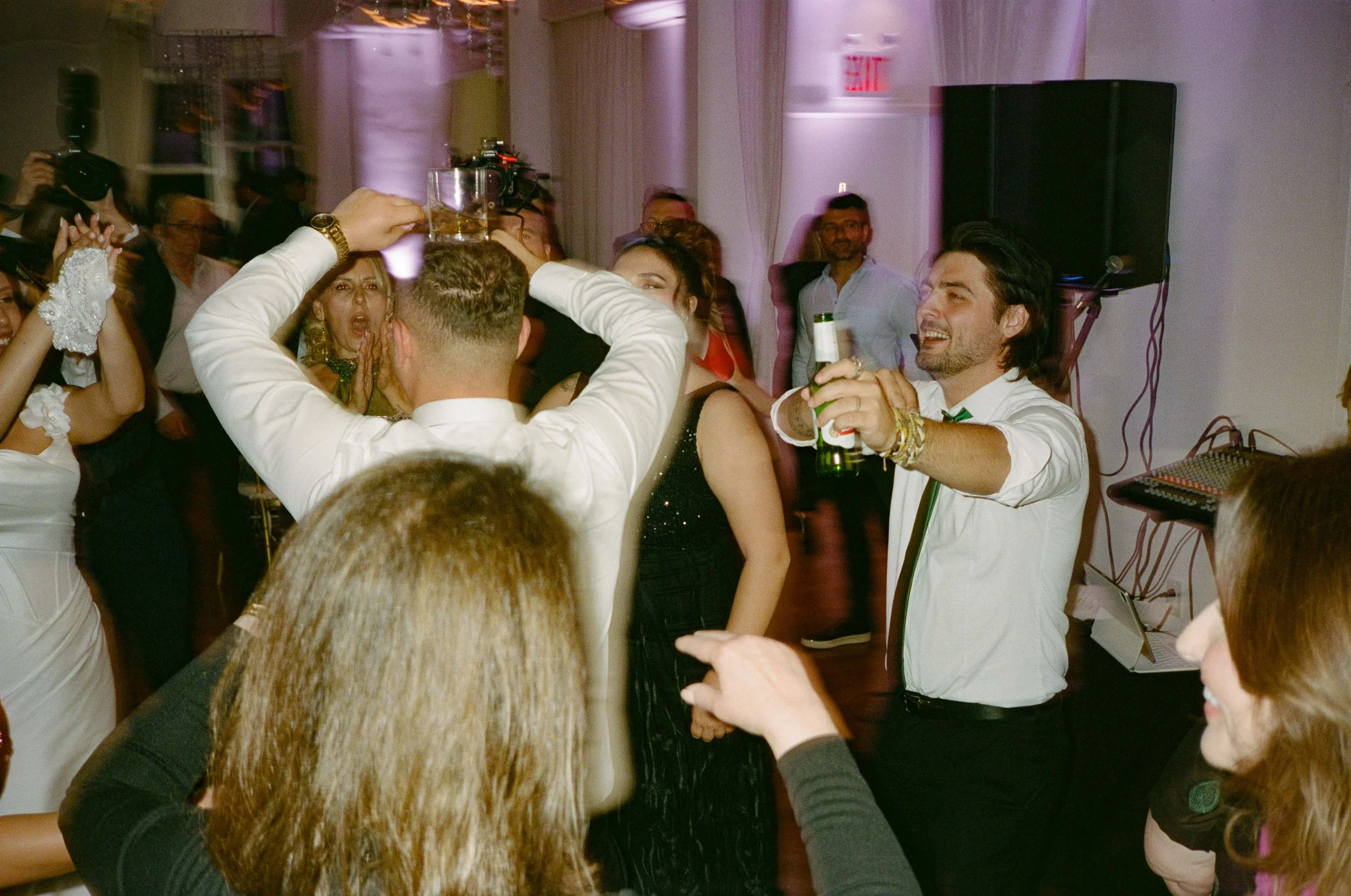 A group of people dancing and celebrating at a party or wedding reception, with drinks in hand and enjoying themselves.