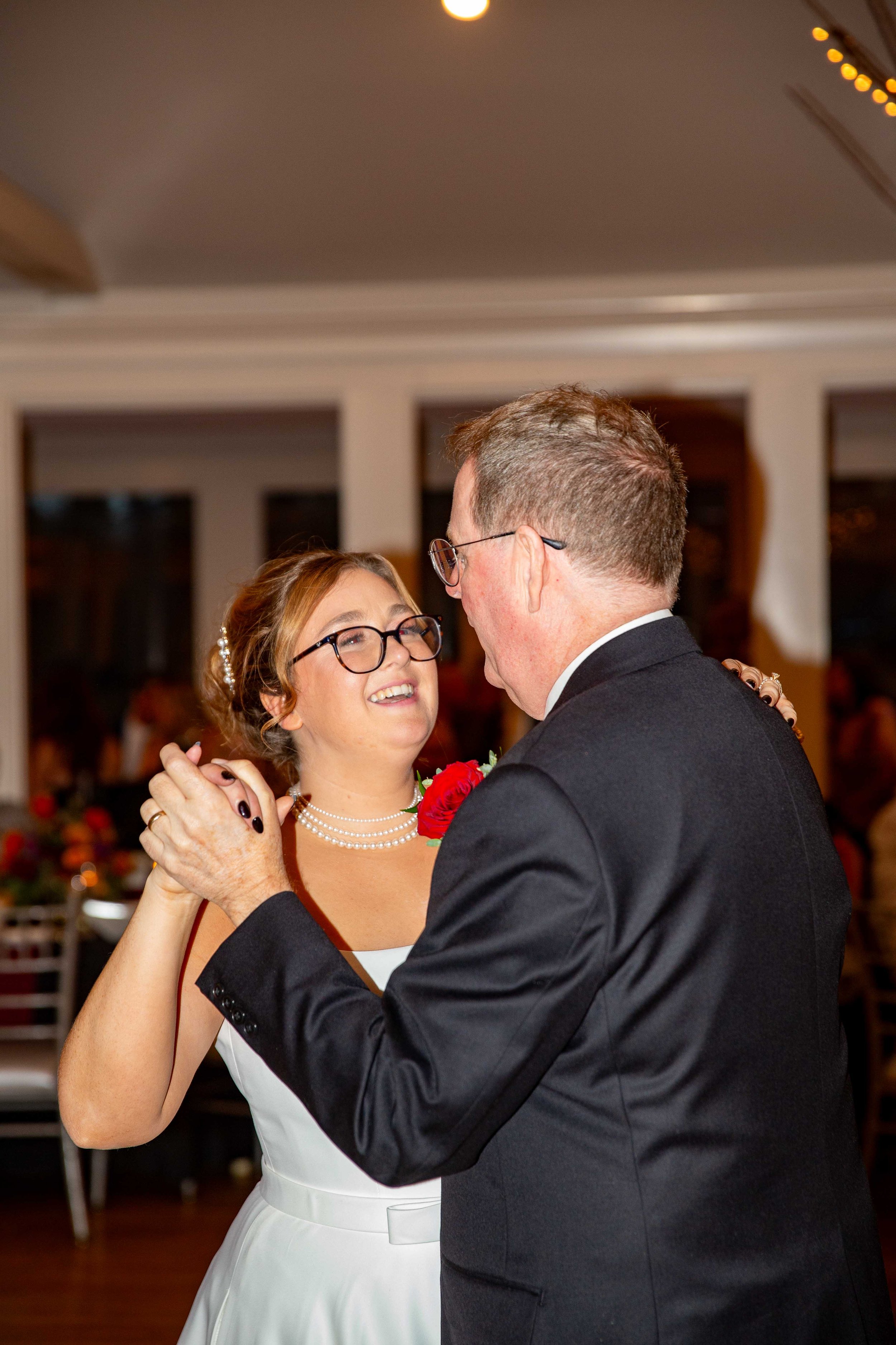 A woman in a white dress and glasses dancing with a man in a black suit at a wedding reception.