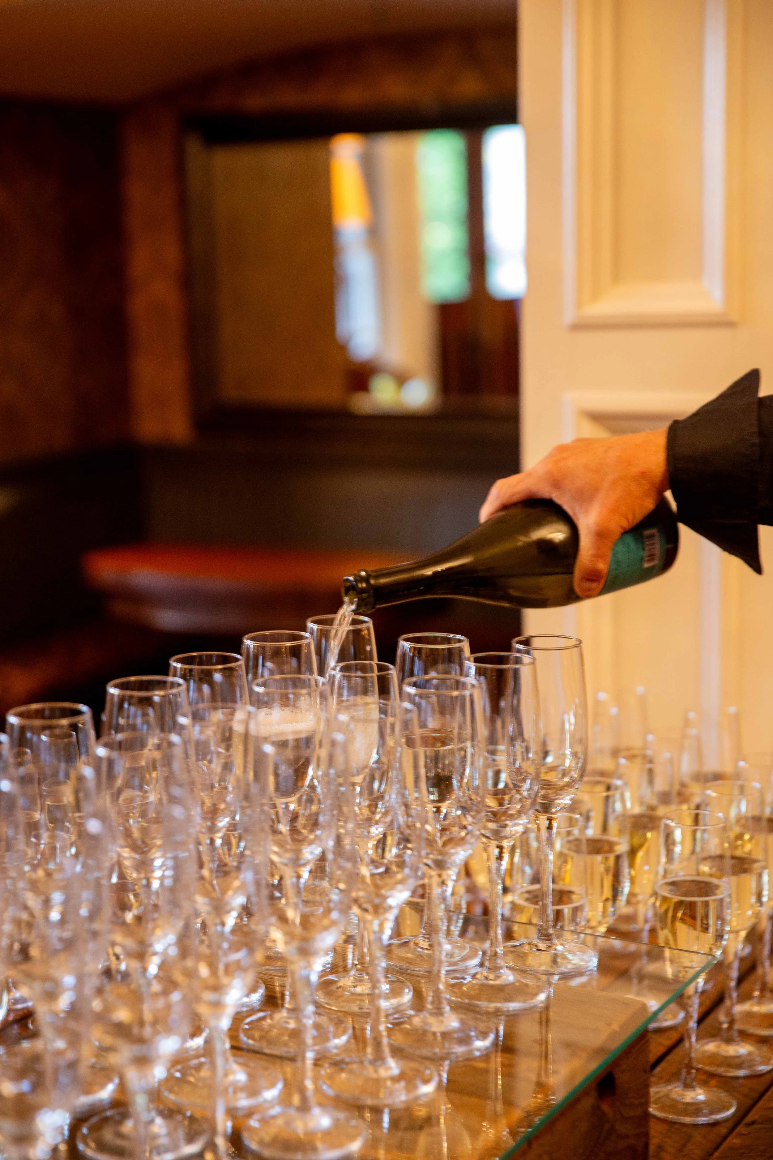 Person pouring champagne into flutes on a table at a celebration or event.