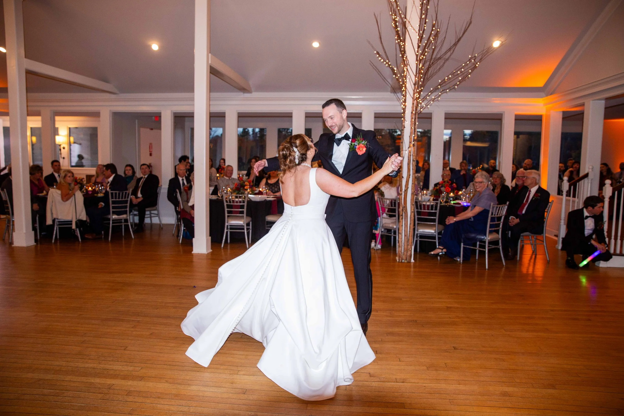 A bride and groom are dancing at their wedding reception inside a decorated event hall while guests watch and celebrate.