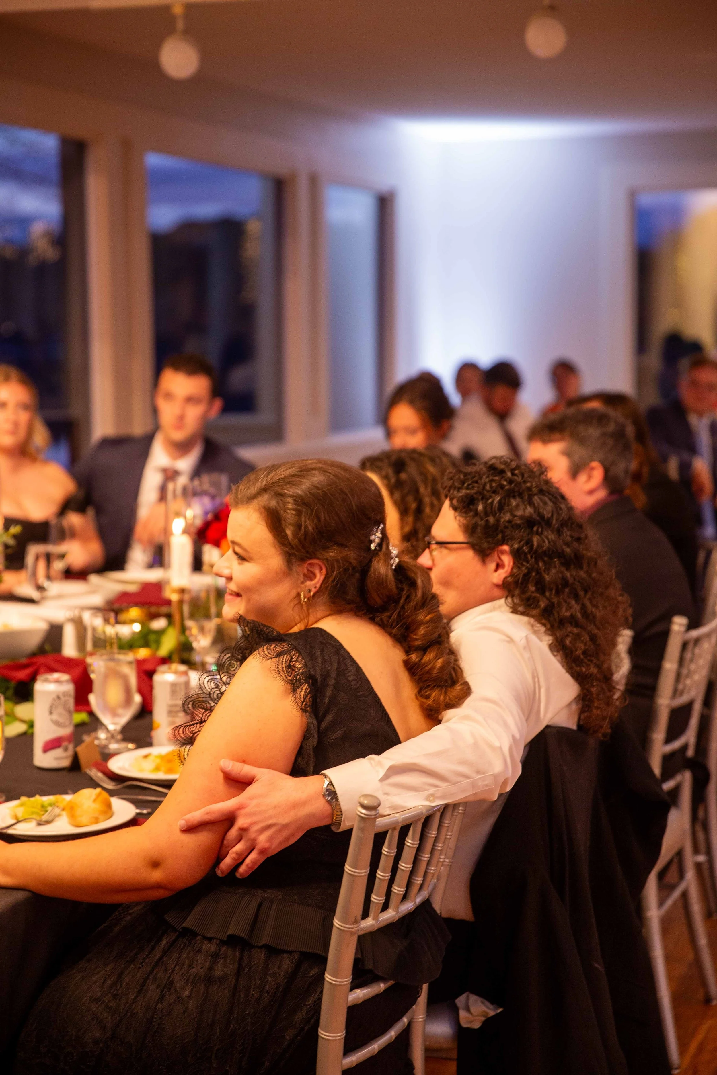 People sitting at a banquet table, smiling and enjoying a celebration, possibly at a wedding or formal dinner event.