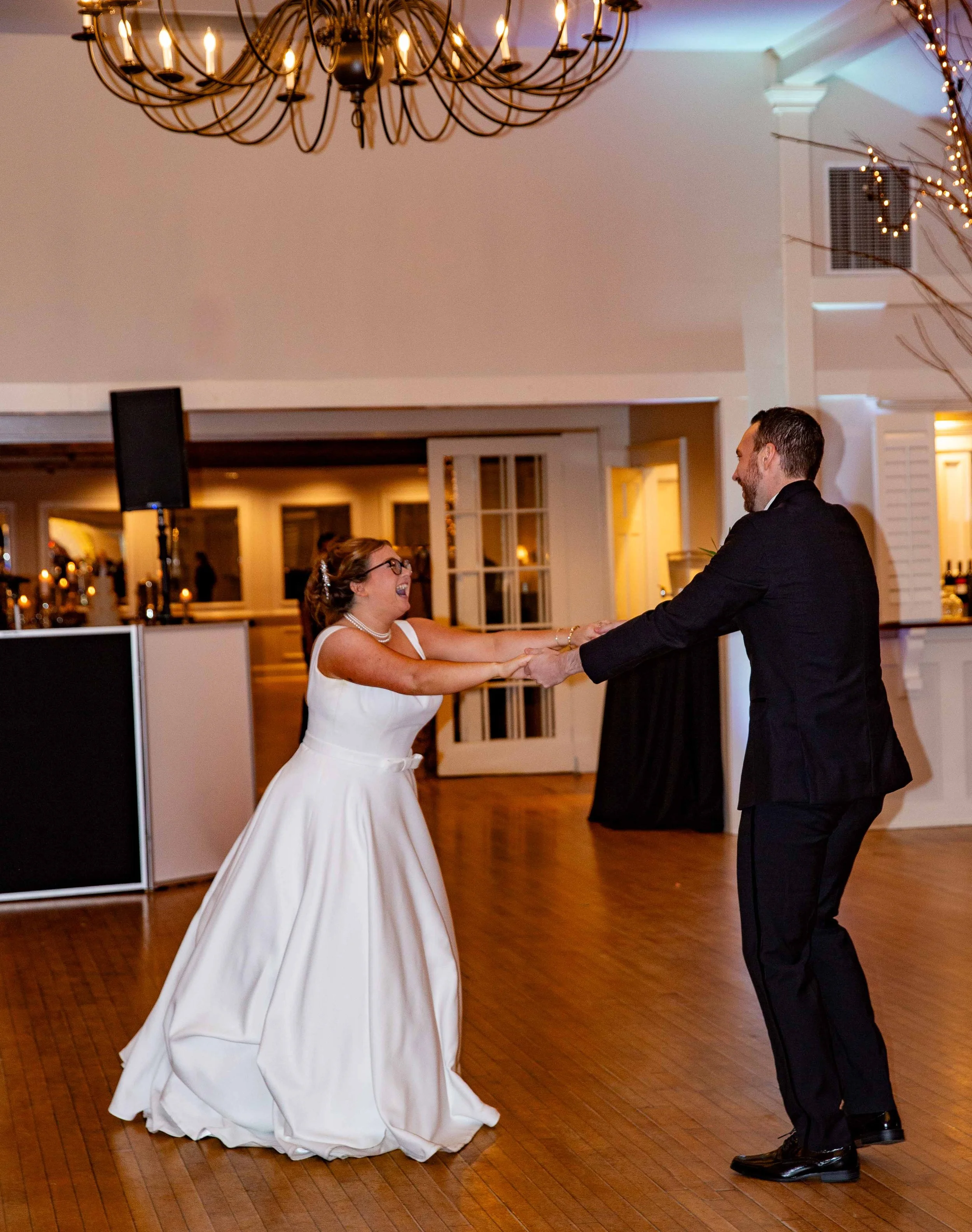 A bride and groom dancing together at a wedding reception in a decorated venue with warm lighting.