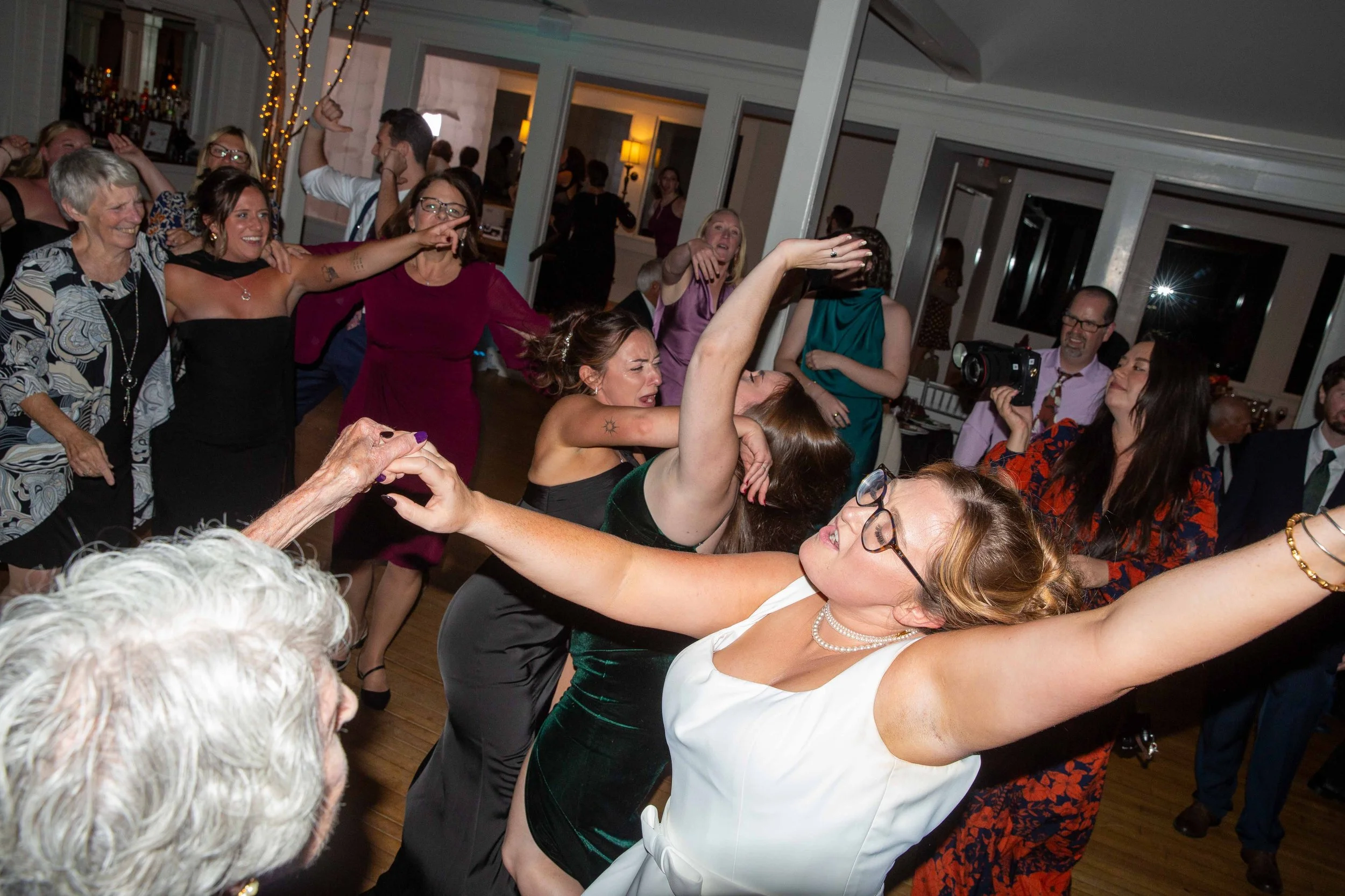 People dancing and celebrating at a party, with some holding hands and others dancing closely, in a lively indoor setting.