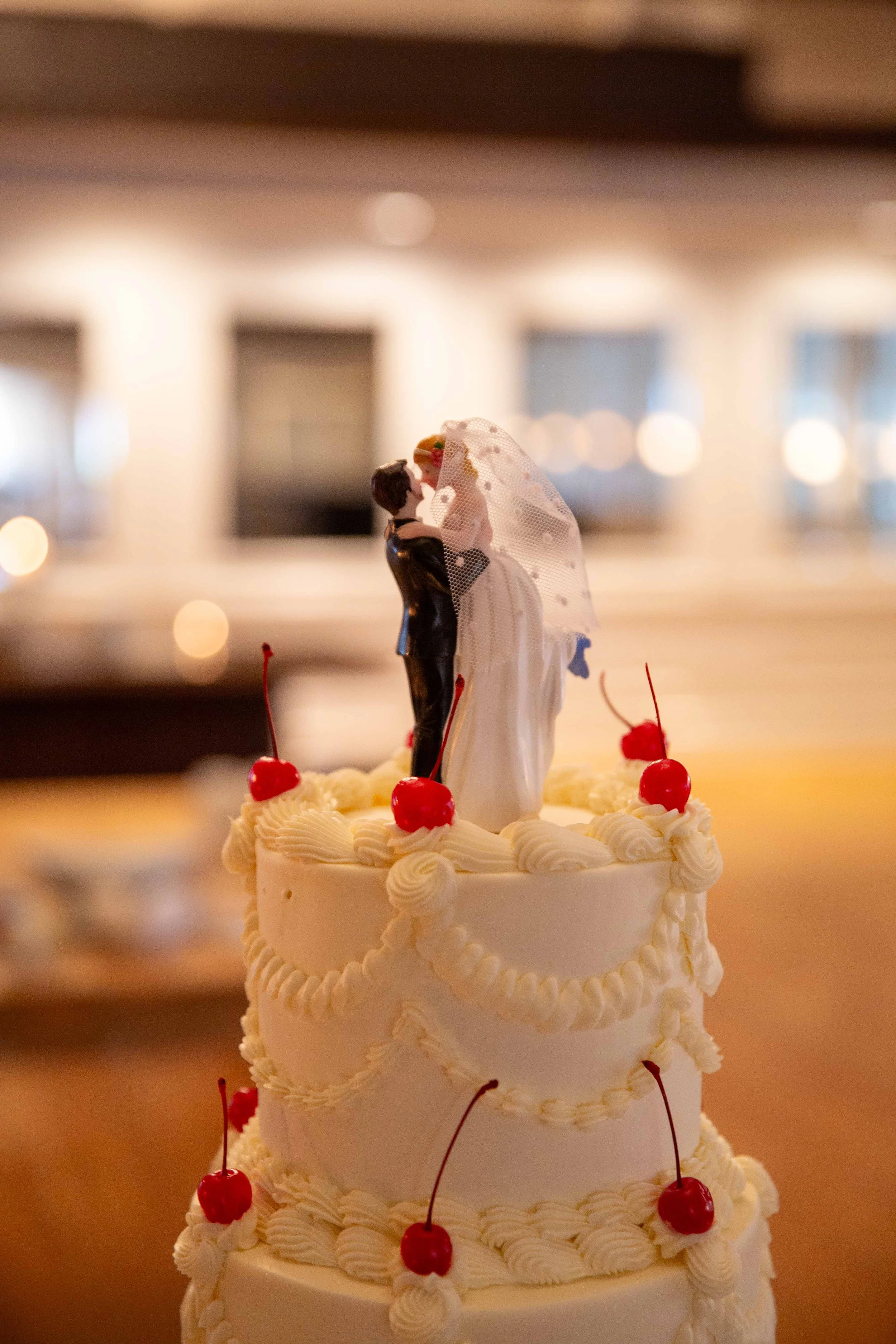 A wedding cake decorated with cherries and white frosting, topped with a figurine of a bride and groom.