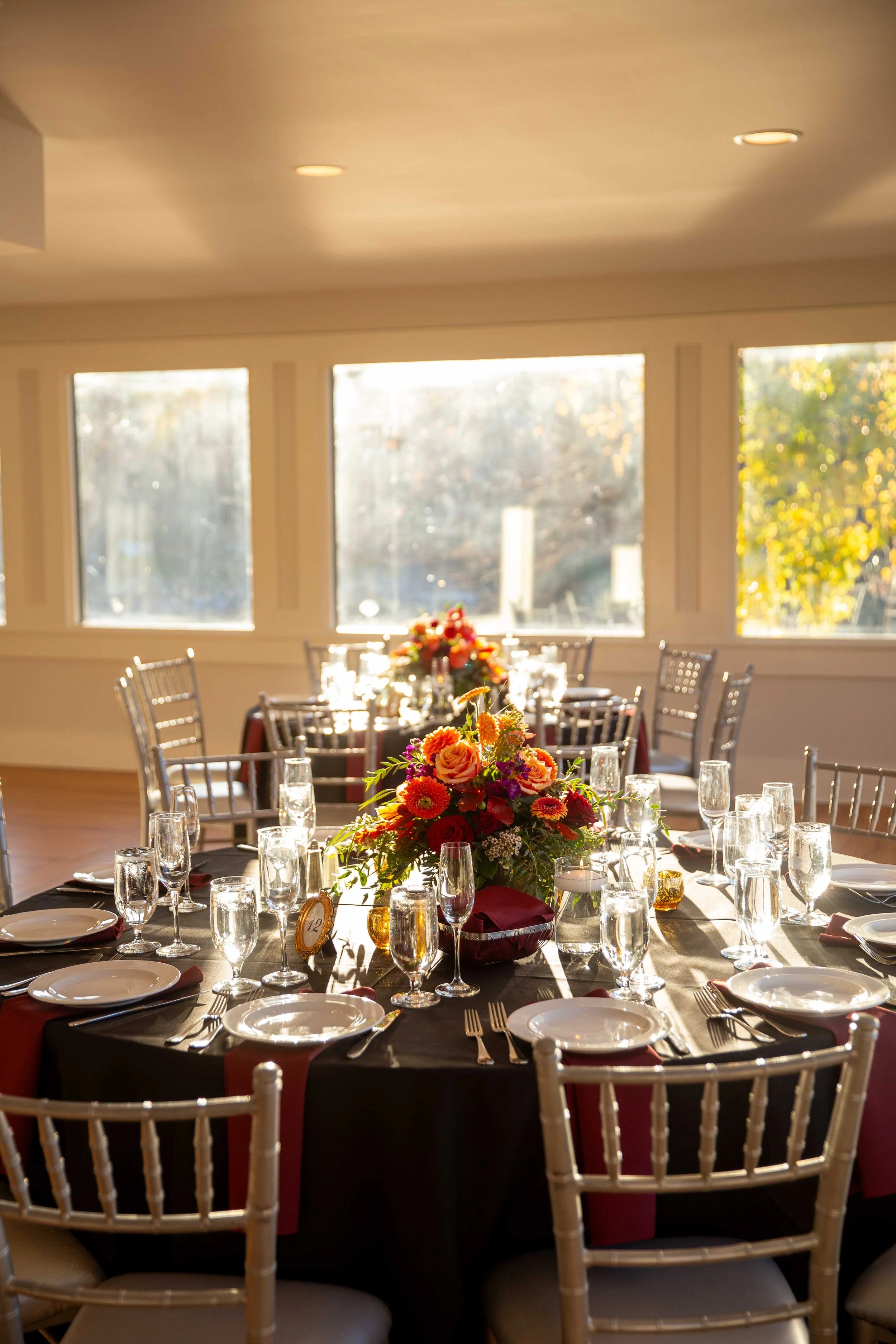 Elegant banquet table set for a celebration with a floral centerpiece, champagne glasses, plates, and silverware in a sunlit room.