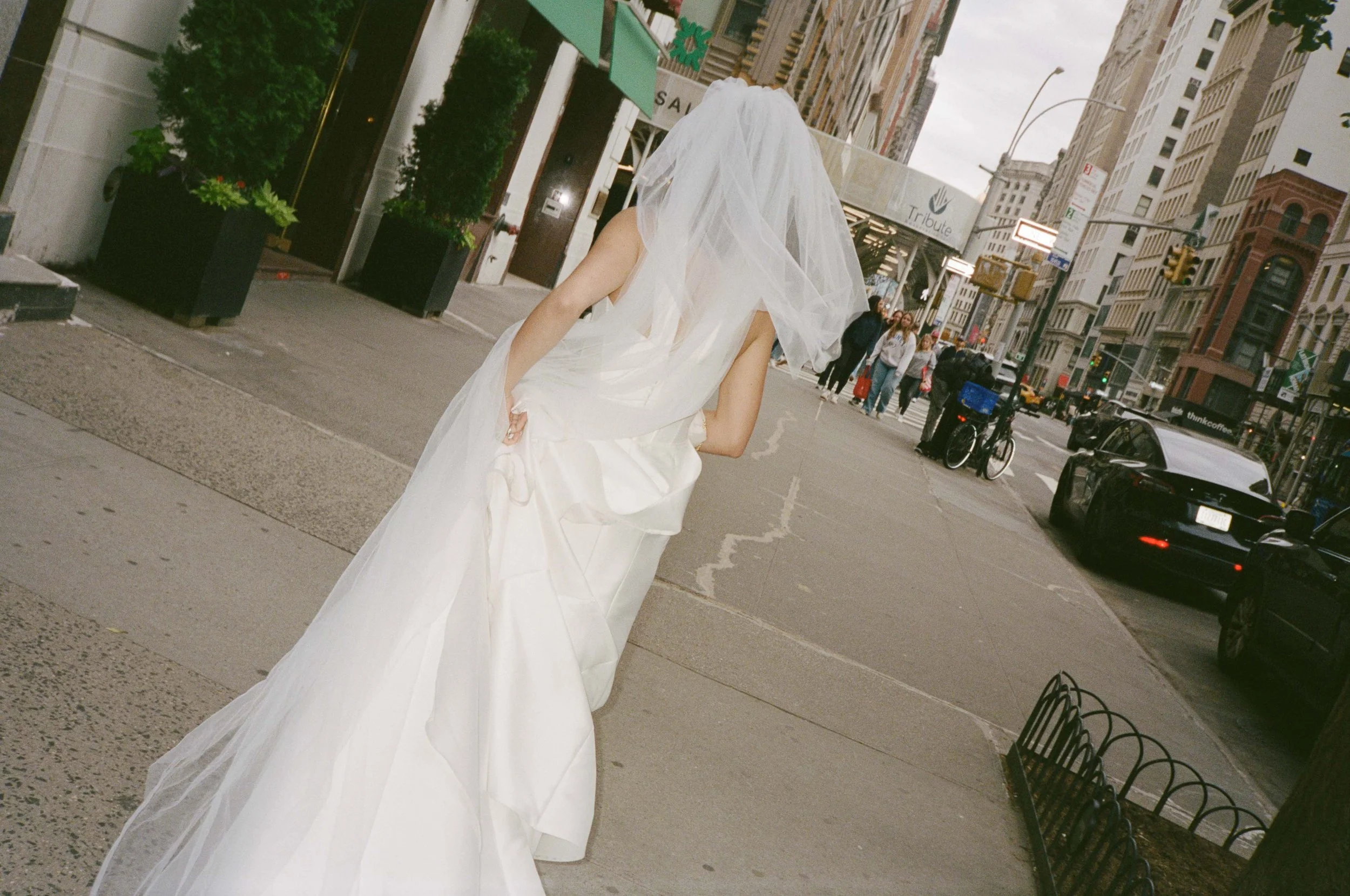 A woman in a white wedding dress and veil walking on a city sidewalk