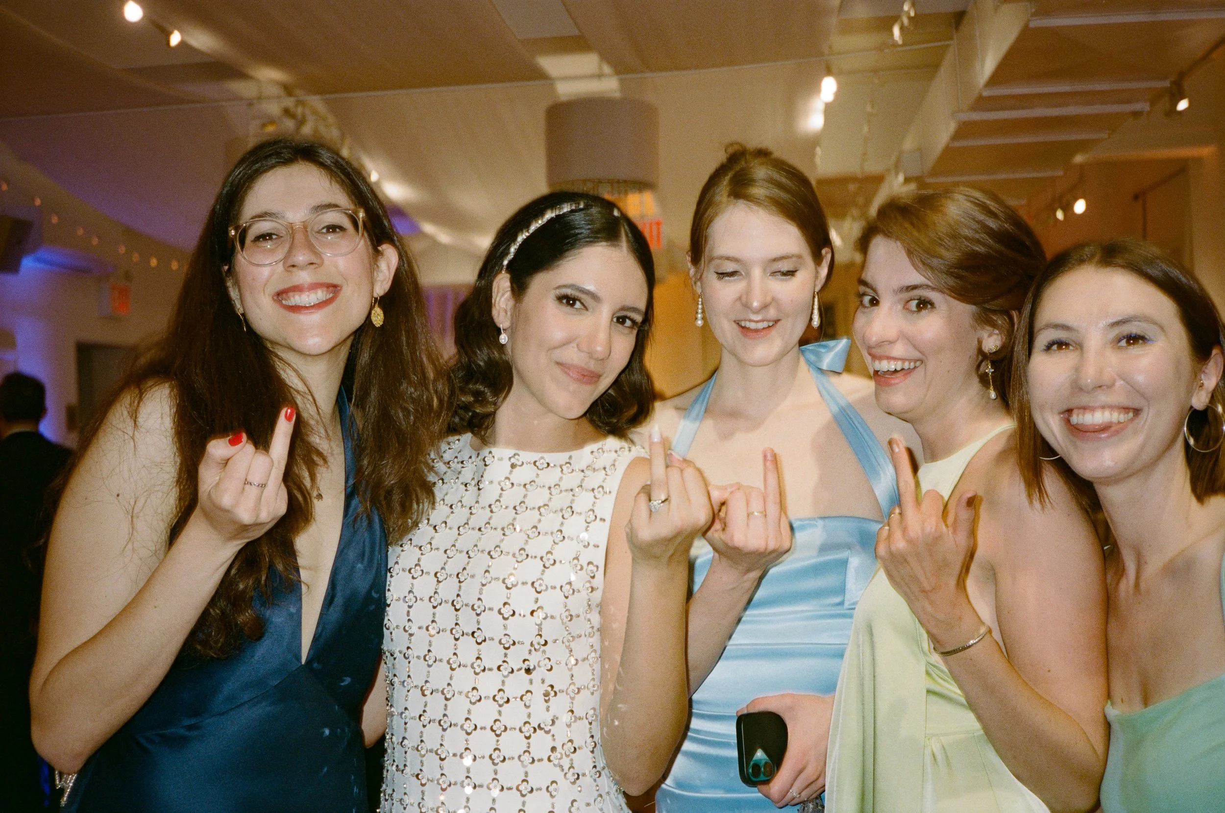 Six women at an event, all smiling and making a rude hand gesture with their middle fingers.