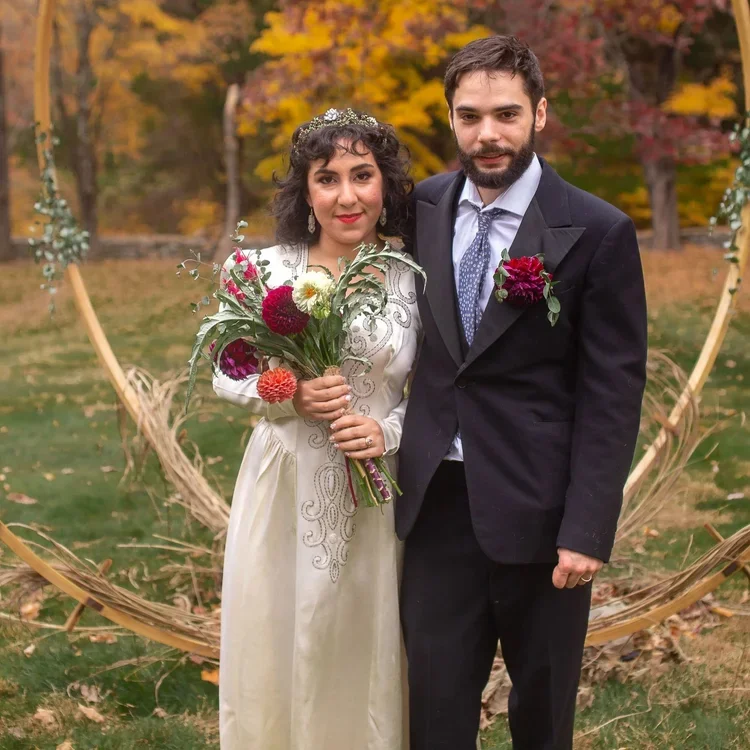 A bride and groom on their wedding day standing outdoors in front of the altar and the bride is holding a bouquet.