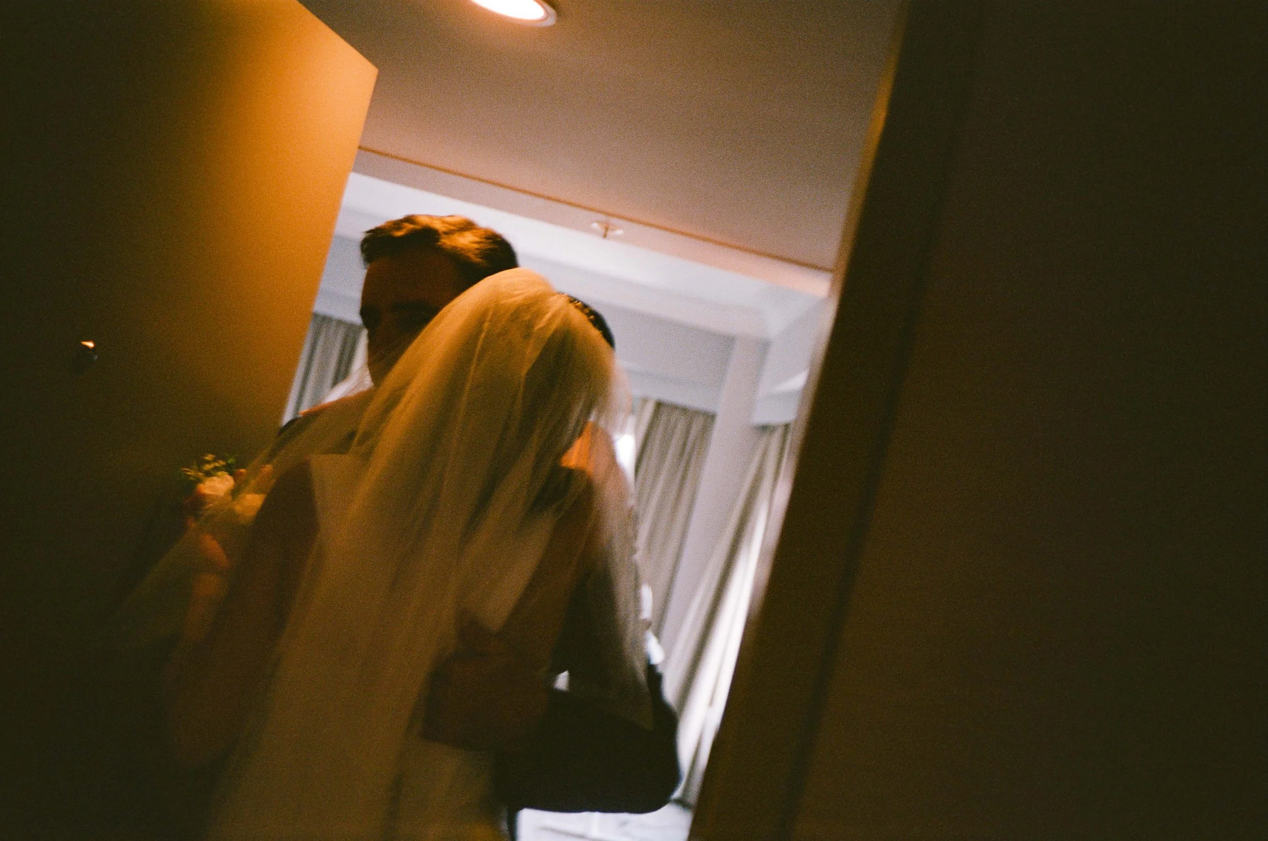 A woman in a wedding dress standing next to a man in a suit, both are partially visible and their faces are not clear, seen through a mirror.