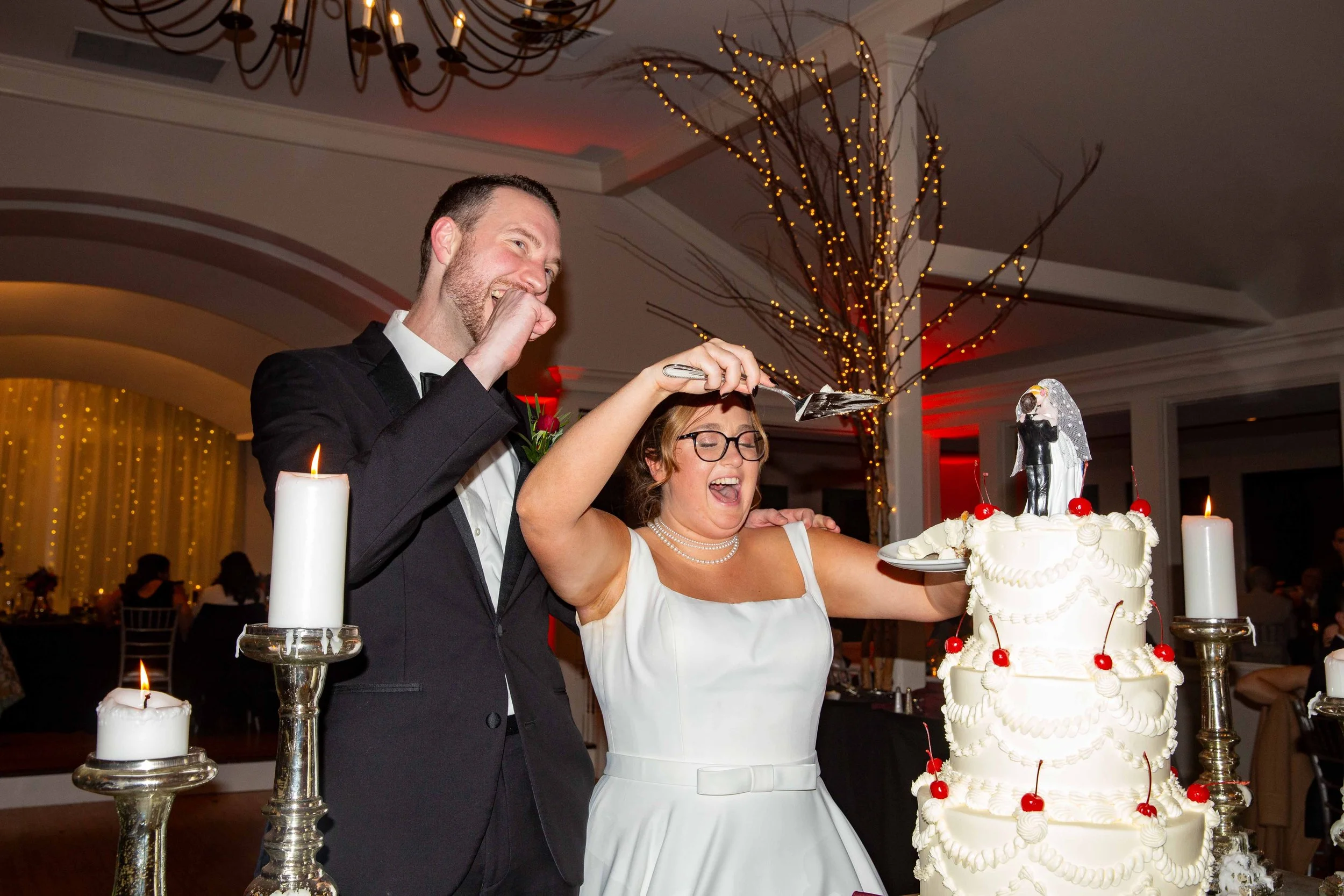 A wedding celebration with a bride and groom cutting a wedding cake with a knife, surrounded by candles, in a decorated banquet hall.