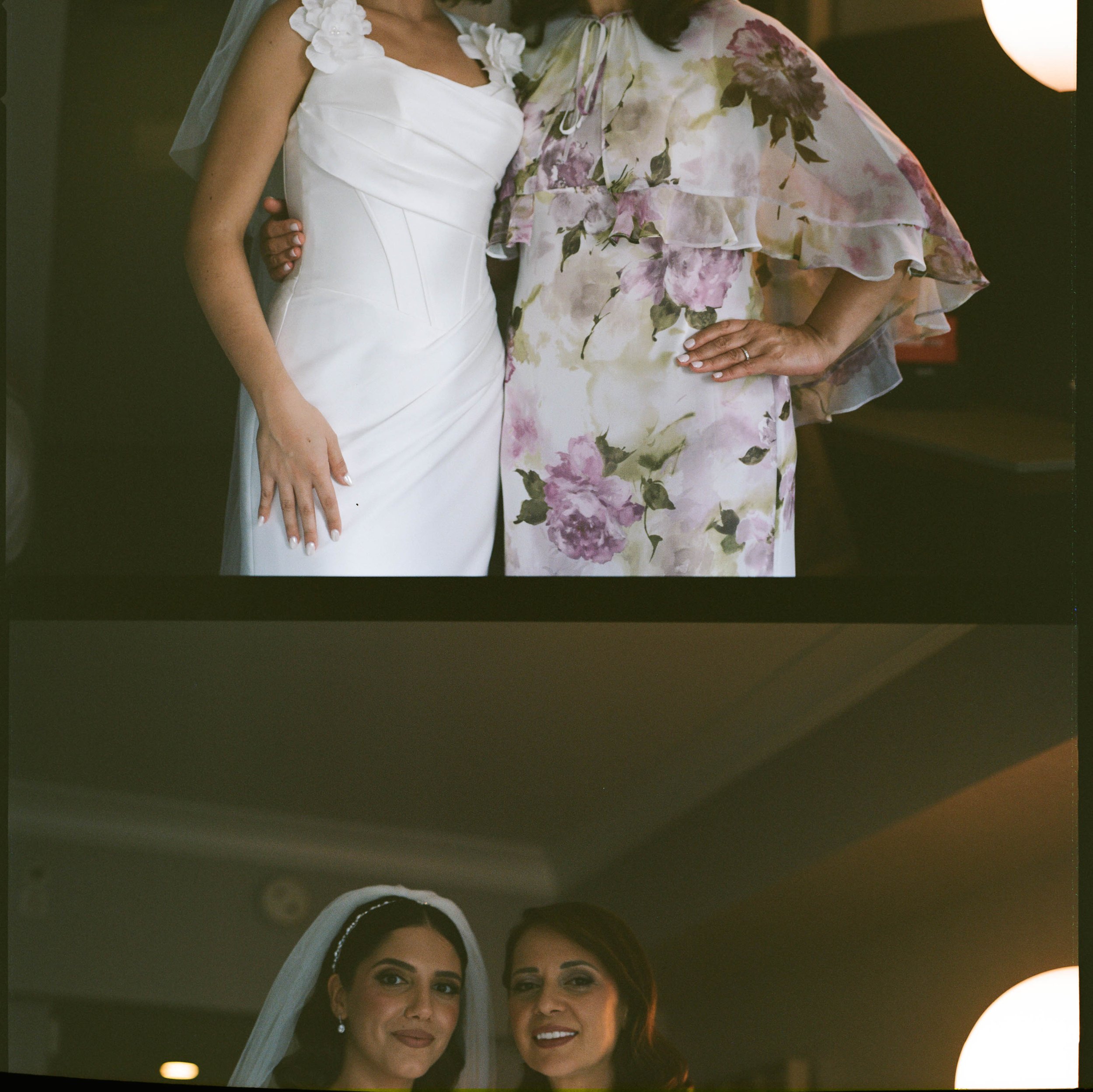 A bride in a white wedding dress standing next to a woman in a floral dress, both partially visible, with the bride wearing a veil and jewelry, all indoors.