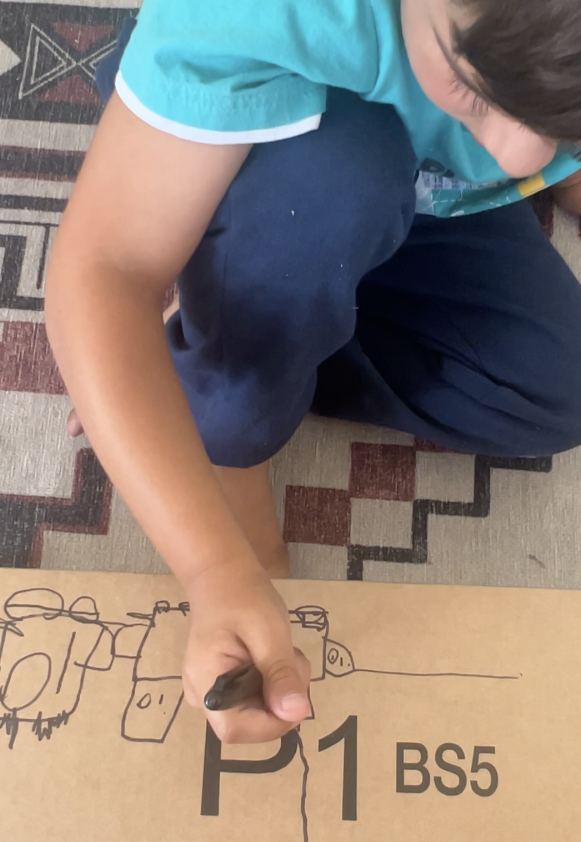 Young child drawing on cardboard as part of a Rooted in Writing hands-on early literacy activity, shared by a parent reviewer from Lakewood, CA.