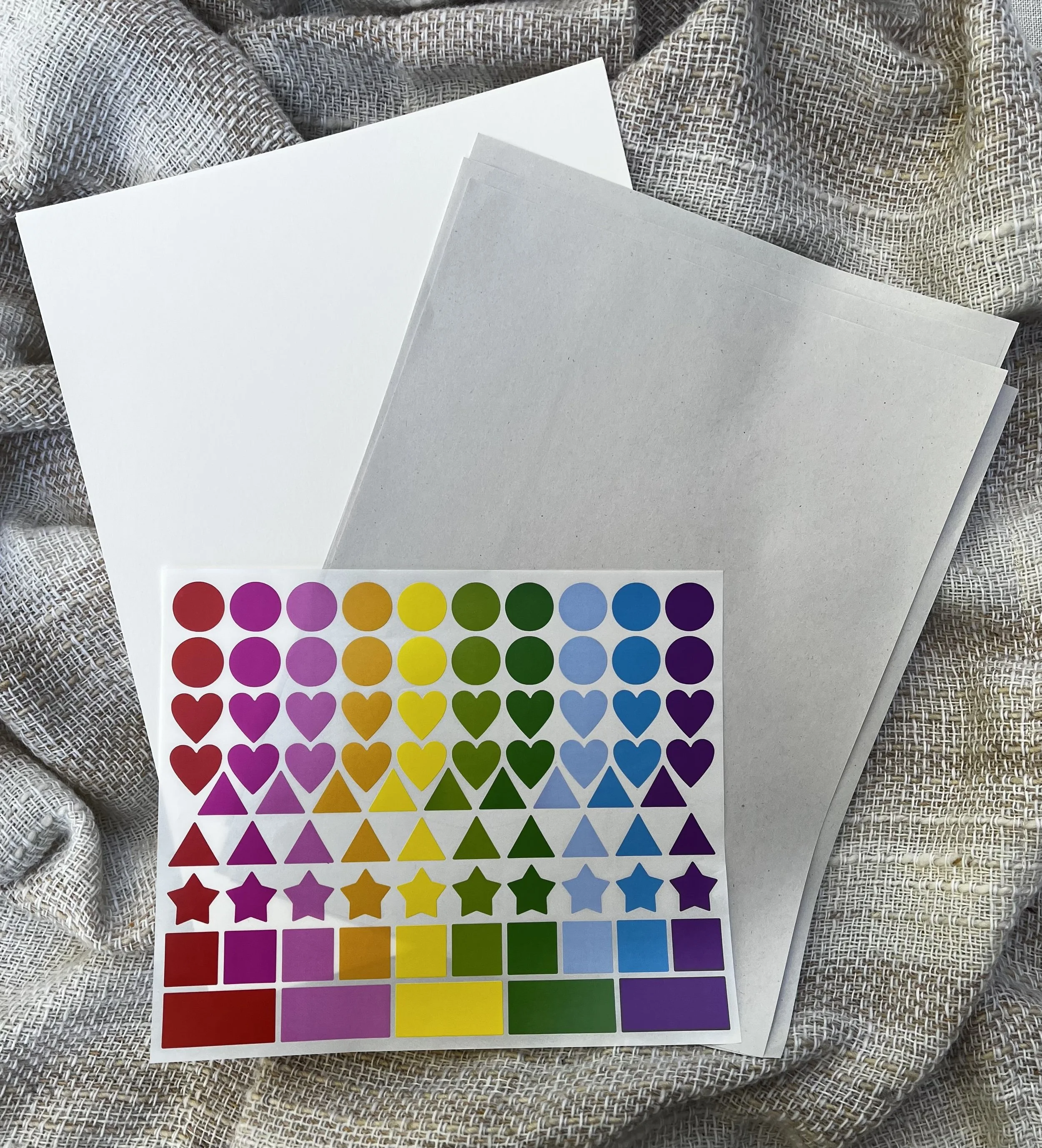 Colorful sticker sheet with various shapes like circles, hearts, stars, and triangles arranged in rows, placed on a fabric surface.