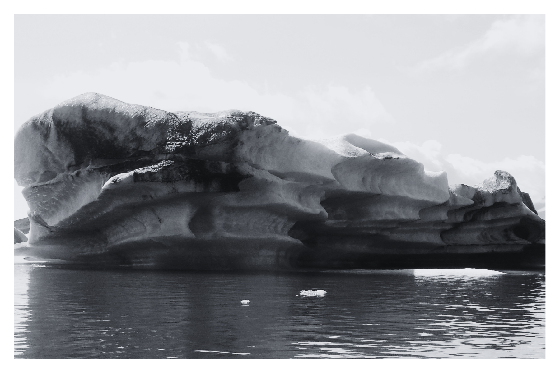 Black and white photo of a large floating ice formation in a body of water with a clear sky in the background.