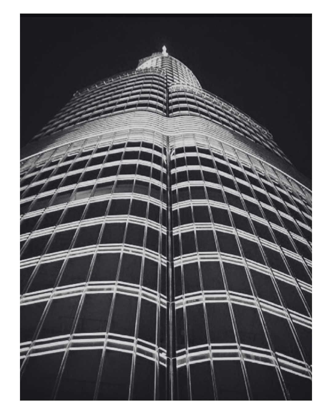 Night view of a tall modern skyscraper with illuminated horizontal and vertical lines on its façade, shot from a low angle.
