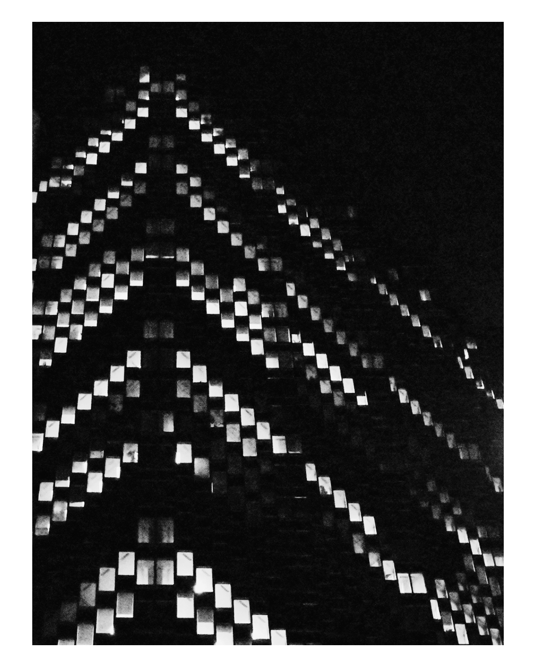 A tall building at night with illuminated windows creating a geometric pattern.