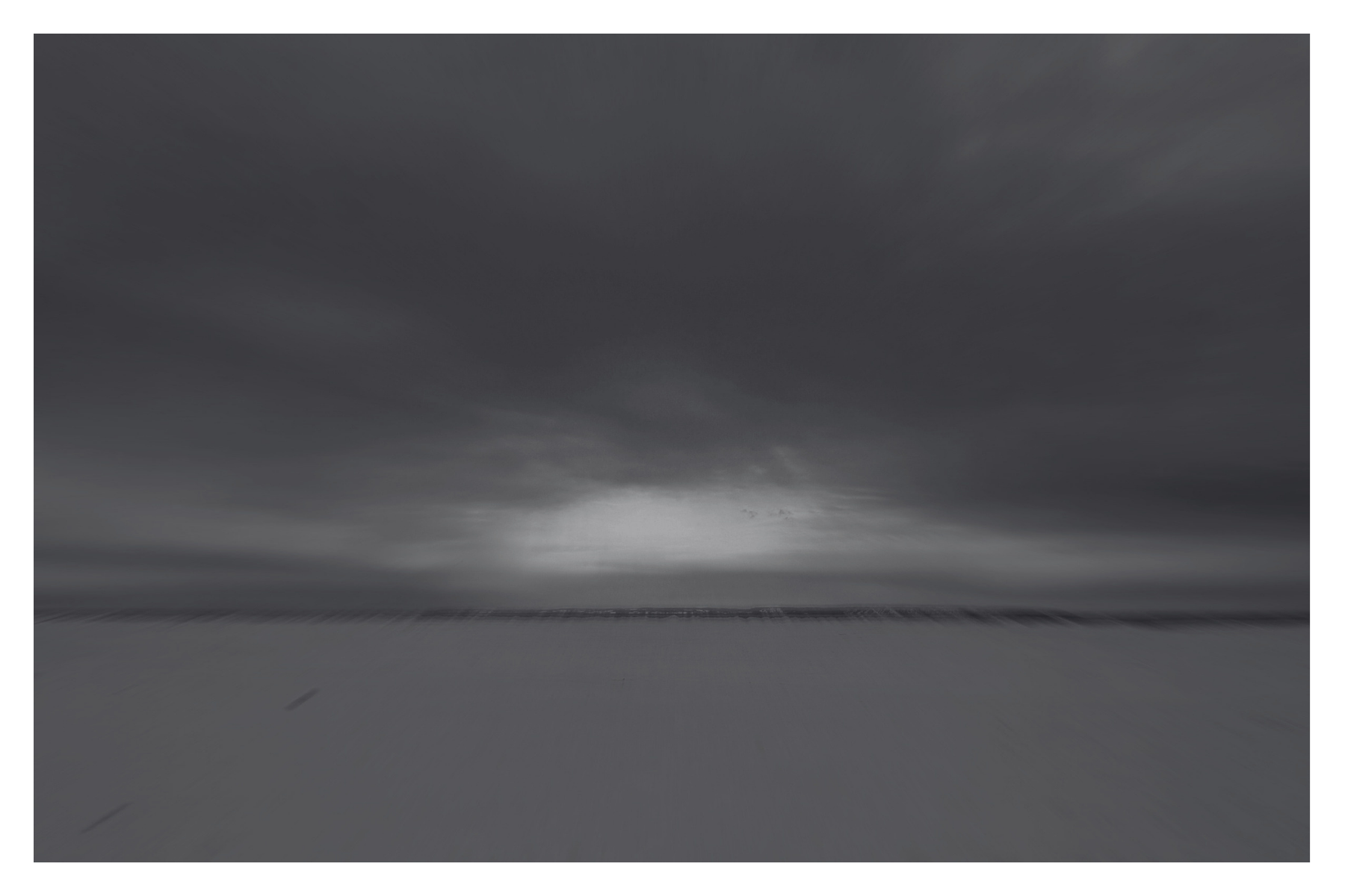 A black and white photo of a vast, empty beach with a dark, cloudy sky overhead.