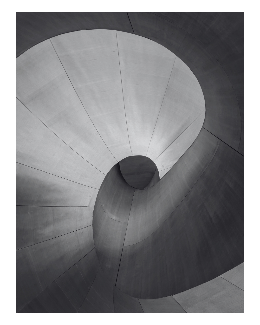 Looking up through a modern concrete spiral staircase, showing the curved walls and the opening at the top.