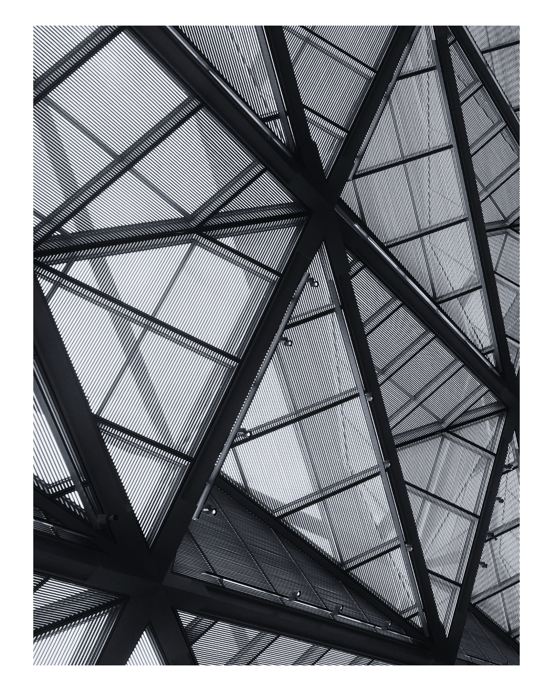 Modern architectural structure with geometric metal framework and glass panels, viewed from below.