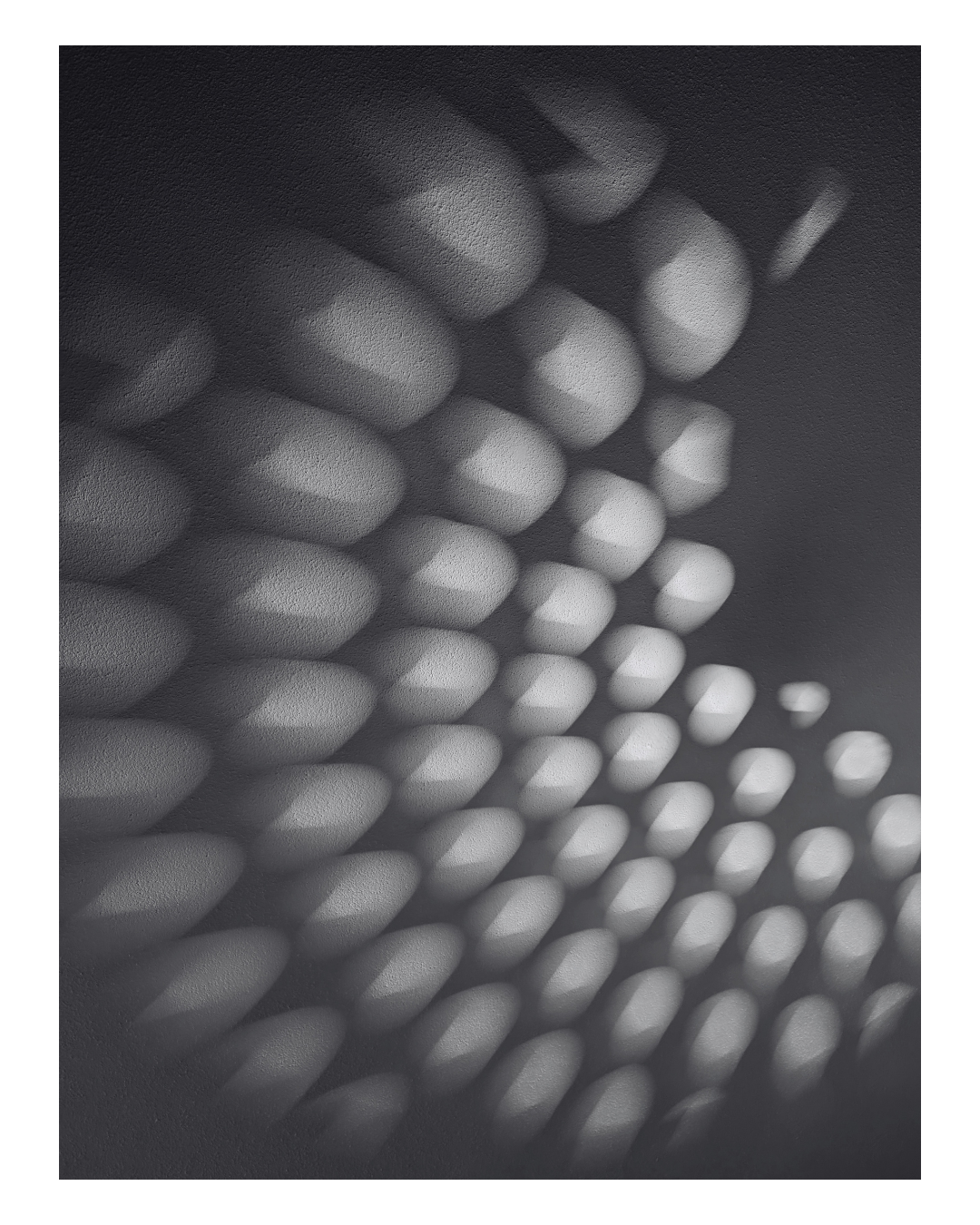Close-up of a textured surface with rounded protrusions casting shadows, creating a pattern of light and dark spots.