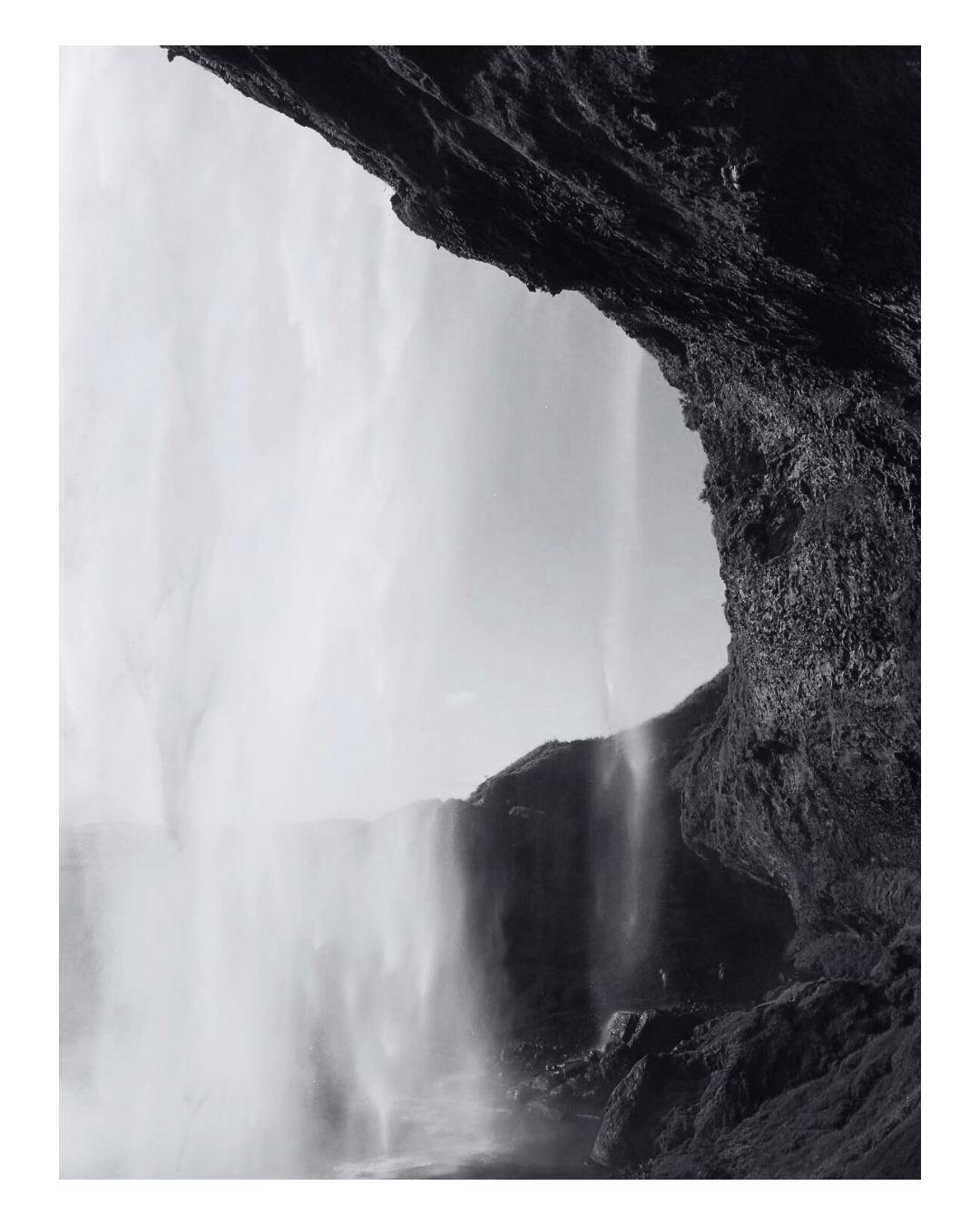 Black and white photograph of a waterfall cascading through a rocky cave or crevice, with mist rising at the base.