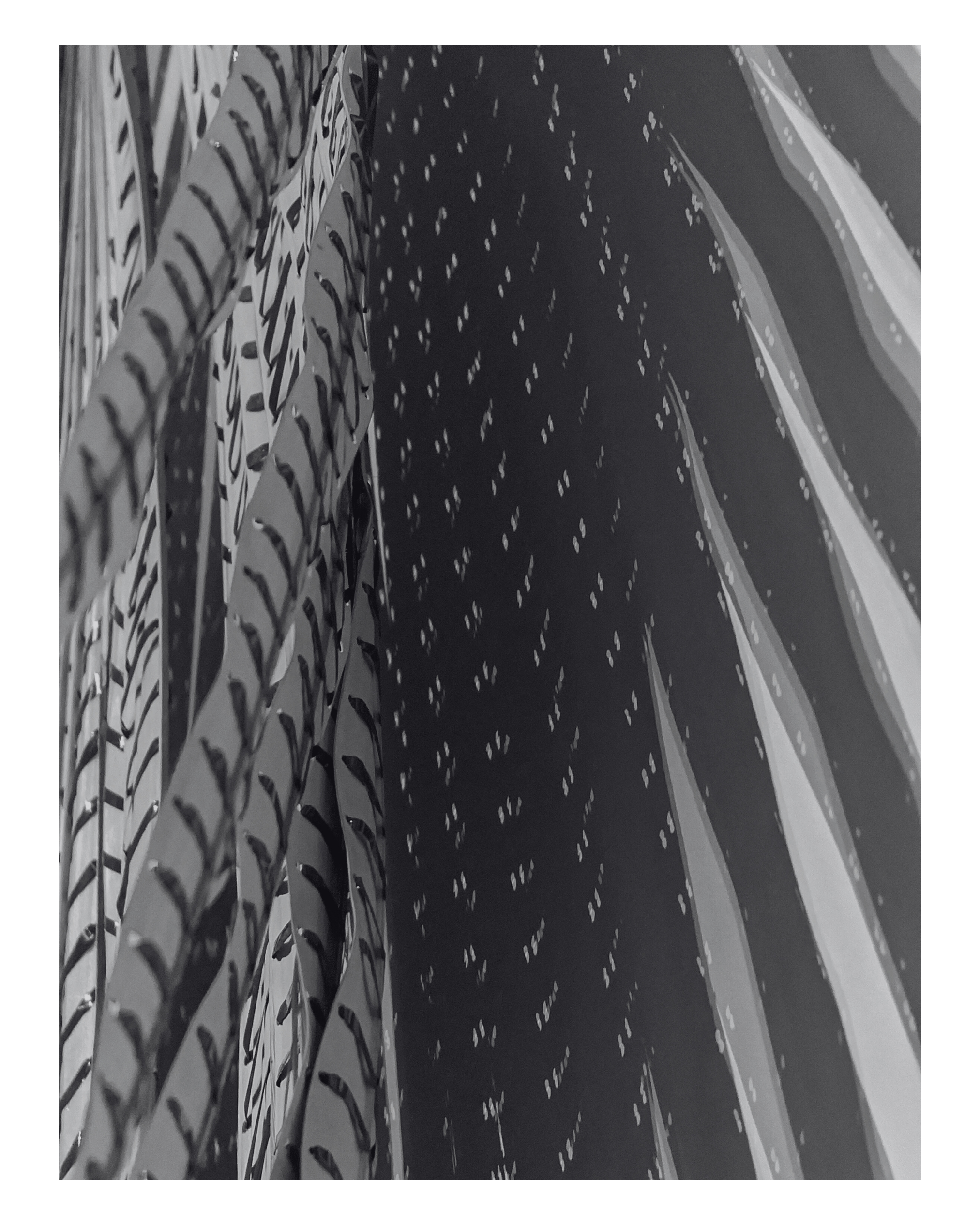 Close-up of metallic, patterned surfaces with abstract, curved designs and small cut-out details, rendered in grayscale.