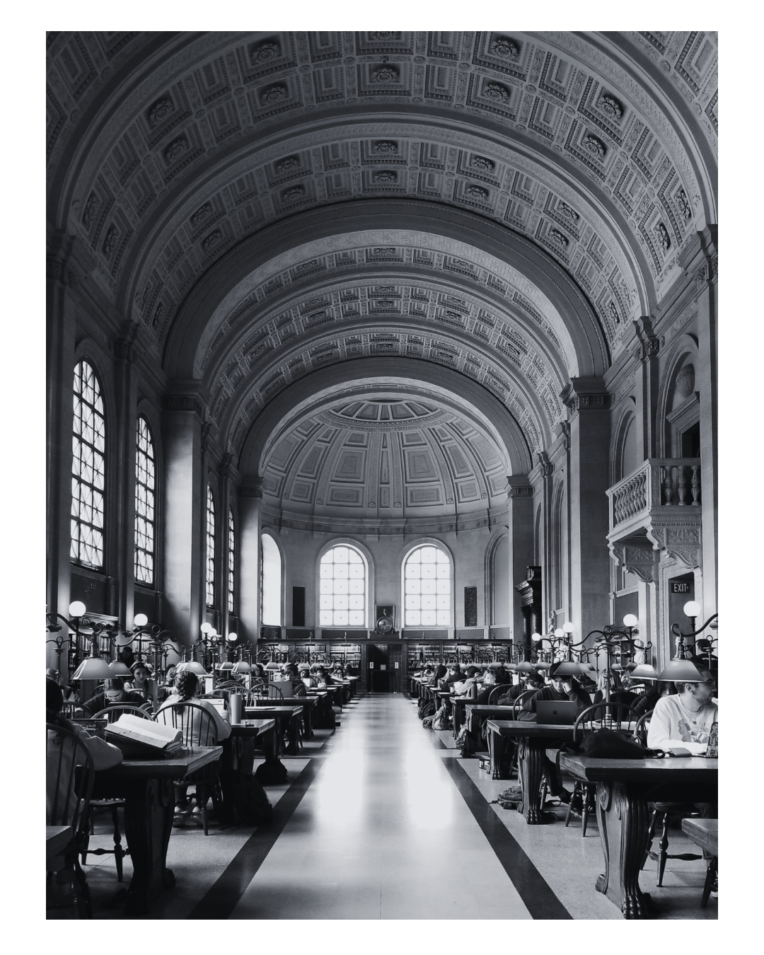 Black and white photo of a large library reading room with high arched ceilings, large windows, and rows of people studying or reading at wooden desks.