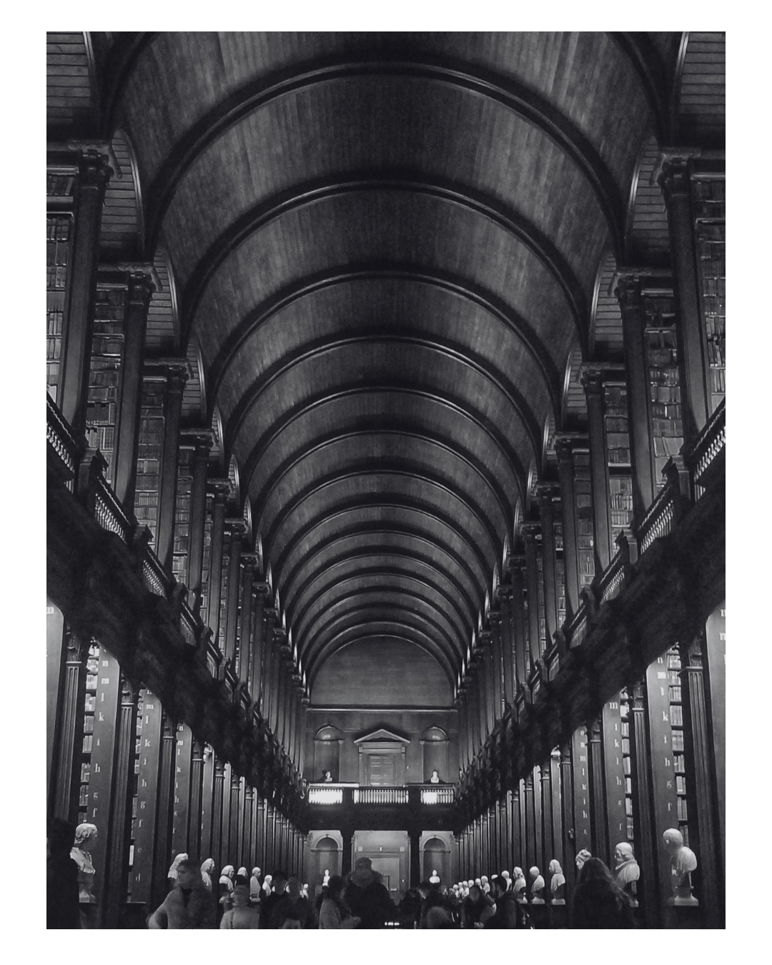 A grand historic library with a high arched ceiling, two levels of bookshelves filled with books, and statues displayed along the walls, with visitors walking through.