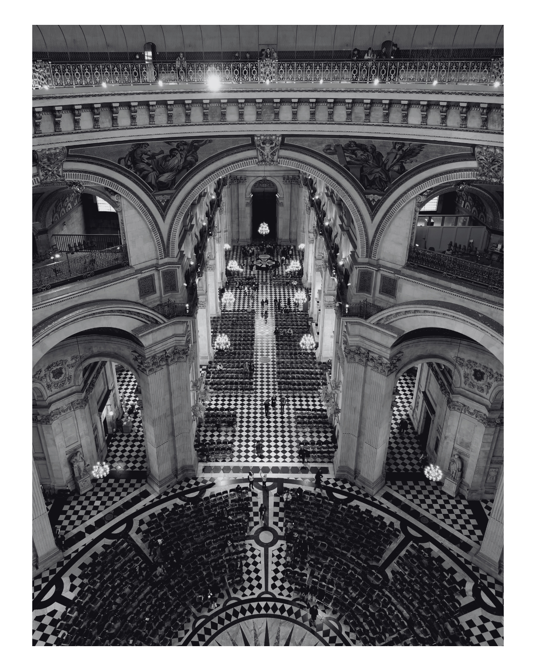 Interior view of a grand, historic building with a high domed ceiling, multiple arched balconies, ornate decorations, and a checkered black and white floor. People are walking and gathering in the spacious central hall.
