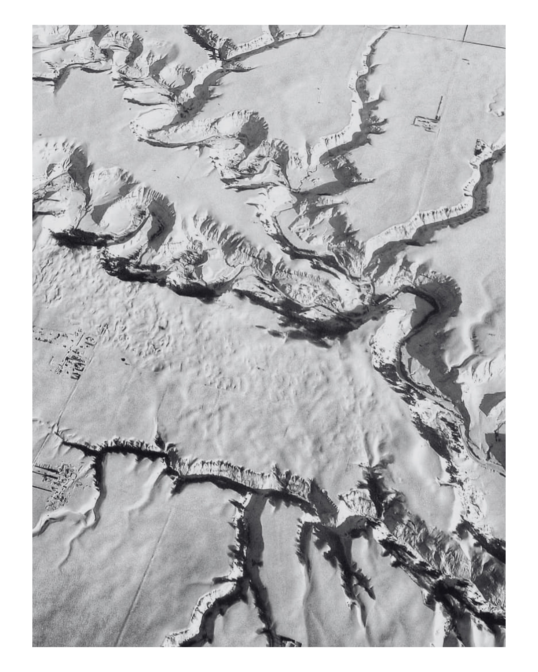 A black-and-white aerial photograph of a snow-covered landscape with winding canyons and a river running through them.