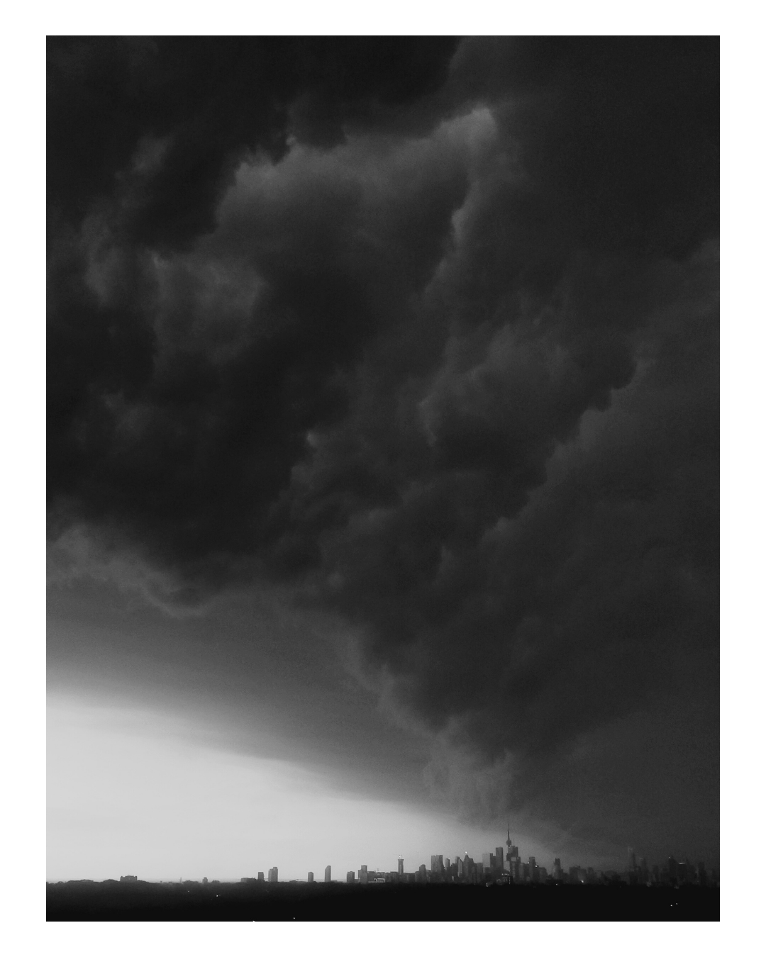 Black and white photograph of a city skyline under a dark, foreboding storm cloud with a funnel cloud forming in the sky.