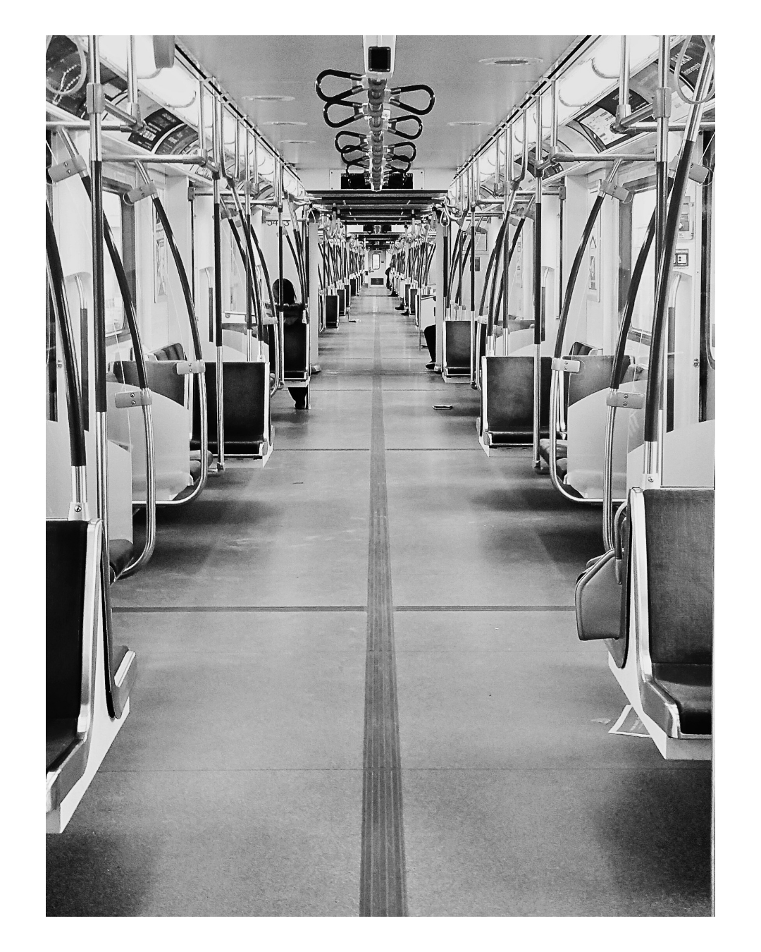 Empty train carriage with seats along the sides, handrails, and hanging straps in black and white.