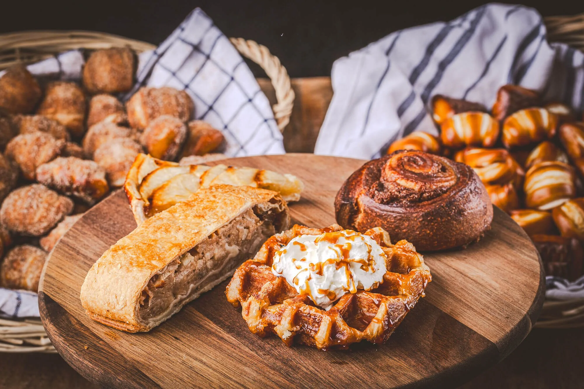 Gâteau aux pommes, tarte, pain à la cannelle, gaufre avec de la crème et du caramel, biscuits de différentes sortes, tous sur une planche en bois