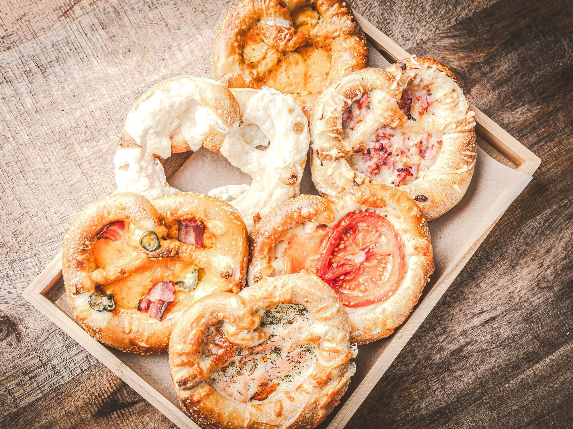 Bretzels salés avec diverses garnitures, présenté dans un panier en bois sur une surface en bois.