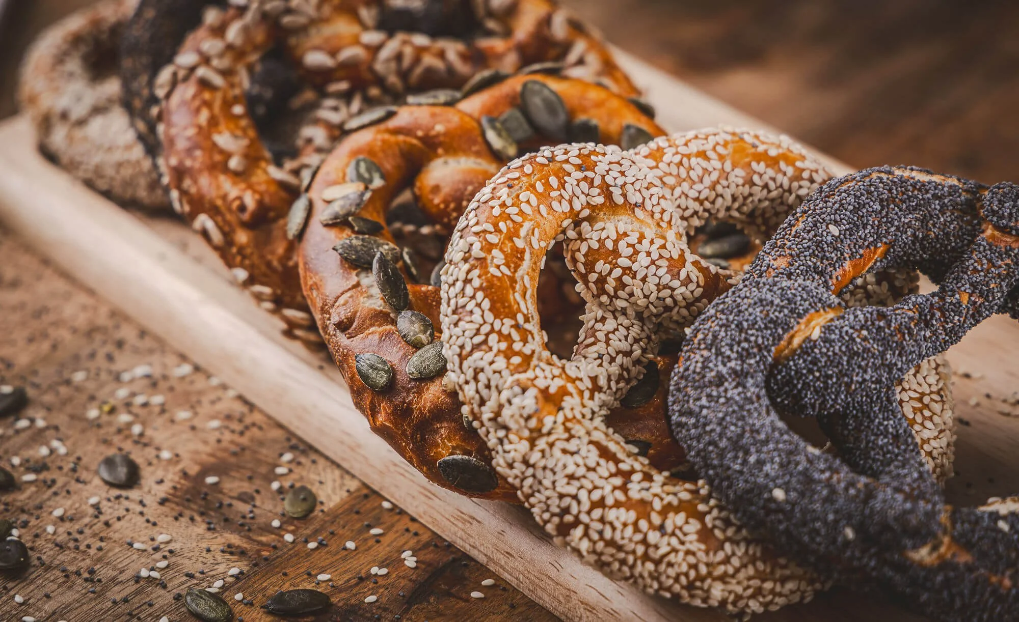 Une rangée de bretzels aux graines de courge, graines de sésame et de pavot sur une planche en bois.