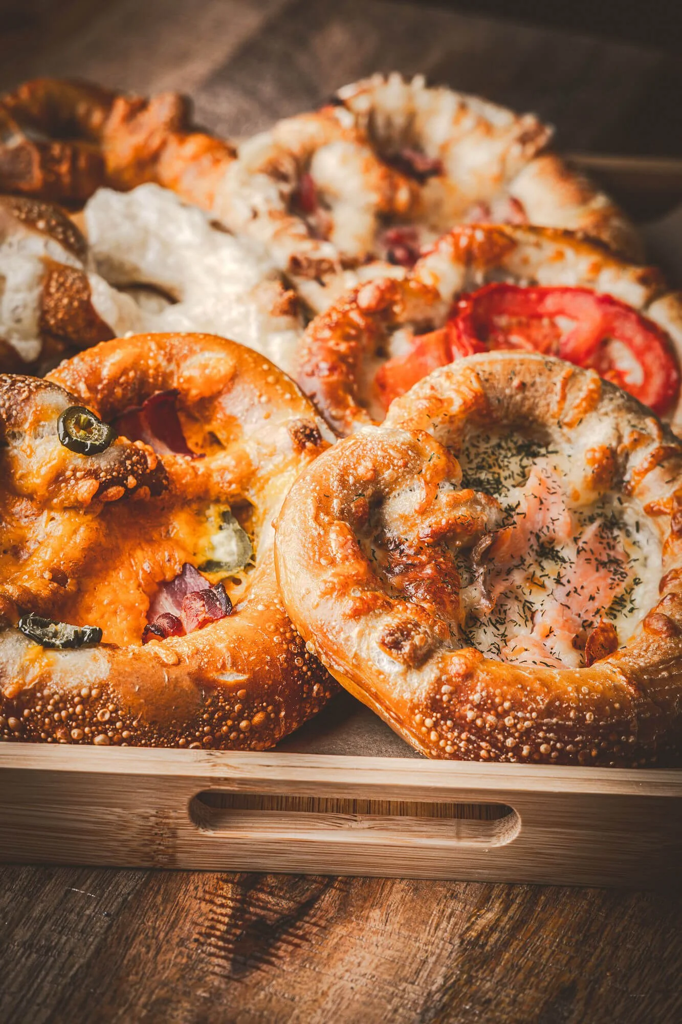 Bretzels gratinés garnis de saumon fumé, crème et lardons, mozzarella sur un plateau en bois