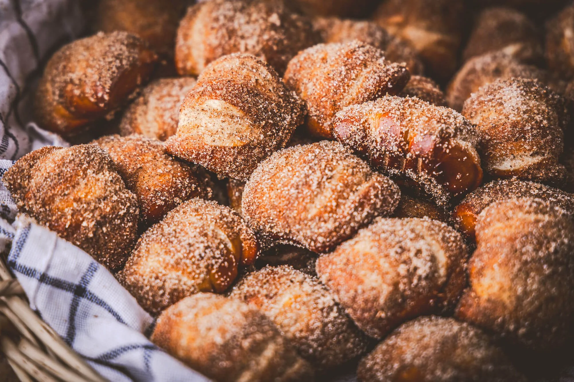 Bouchées de bretzels enrobés de sucre cannelle dans un panier en osier avec une serviette à carreaux blancs et bleus.