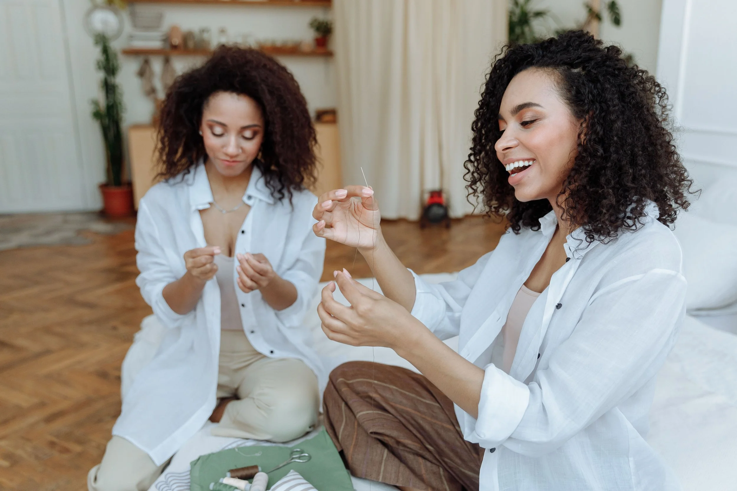 Two women smiling and laughing together while making jewelry during a cozy girls’ night in, surrounded by creative supplies and a warm, relaxed atmosphere.