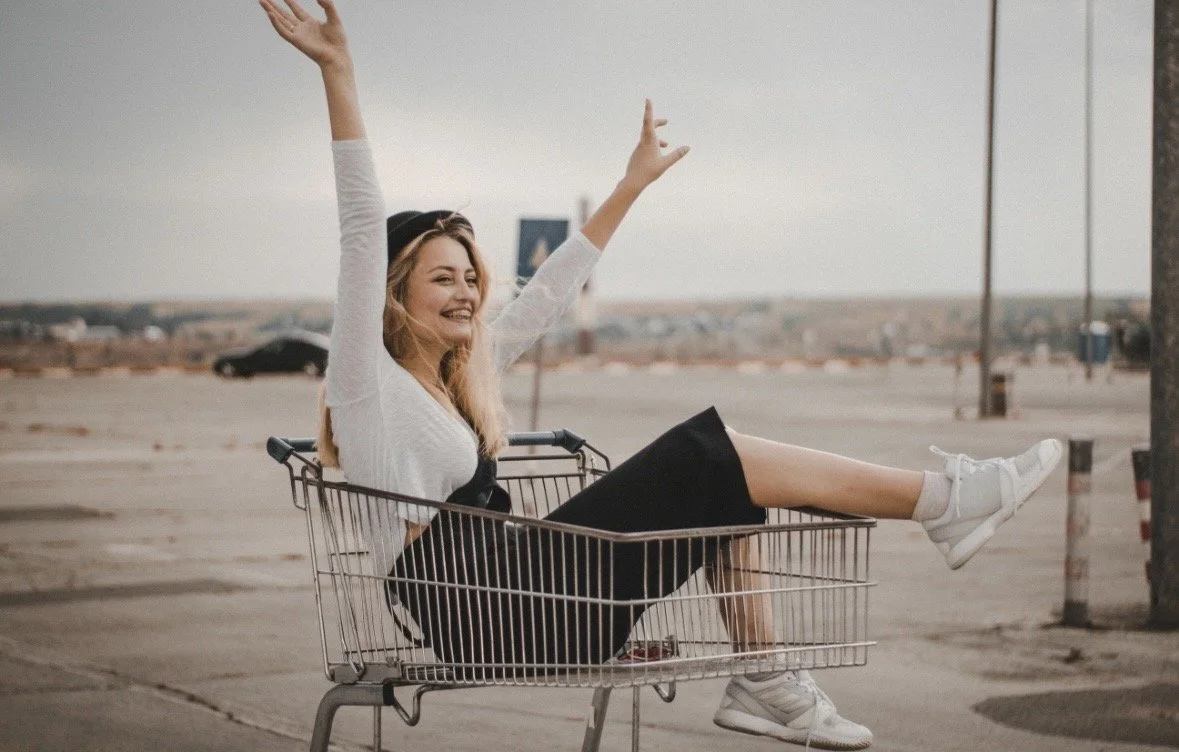 Woman laughing while riding in a shopping cart, capturing the joy, spontaneity, and playfulness often missing from adult life.