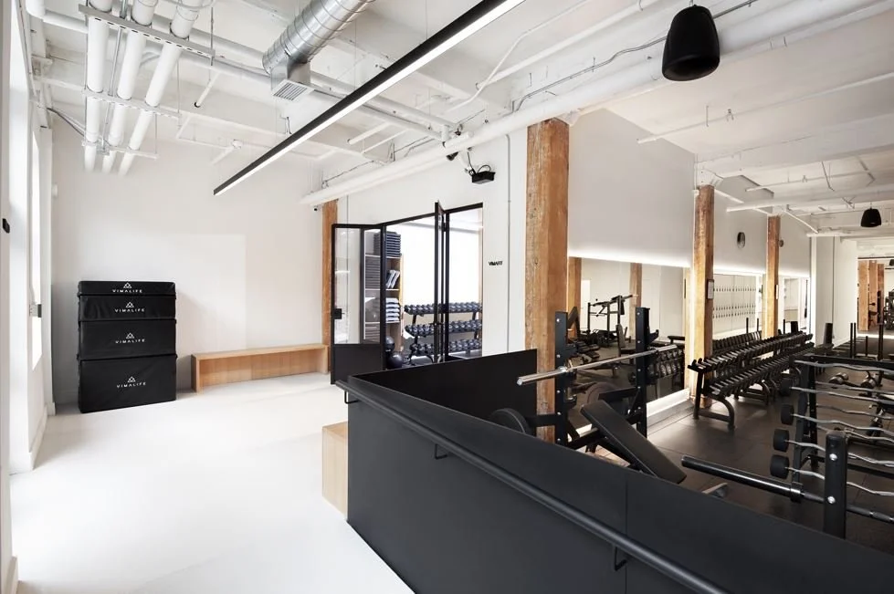 Modern gym with weightlifting equipment, lockers, and training mats in a well-lit, industrial-style space.