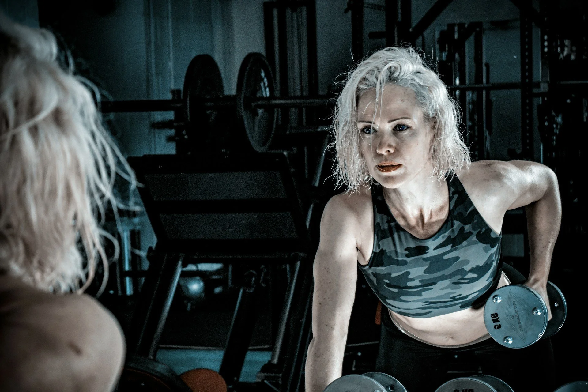 Woman strength training with dumbbells in front of a gym mirror.