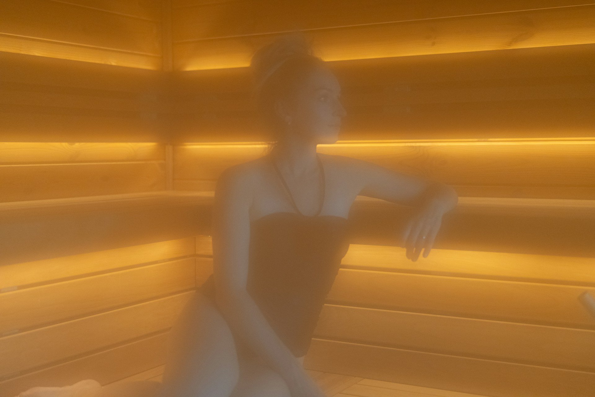 Woman relaxing in a sauna, highlighting heat therapy, stress relief and recovery after training.